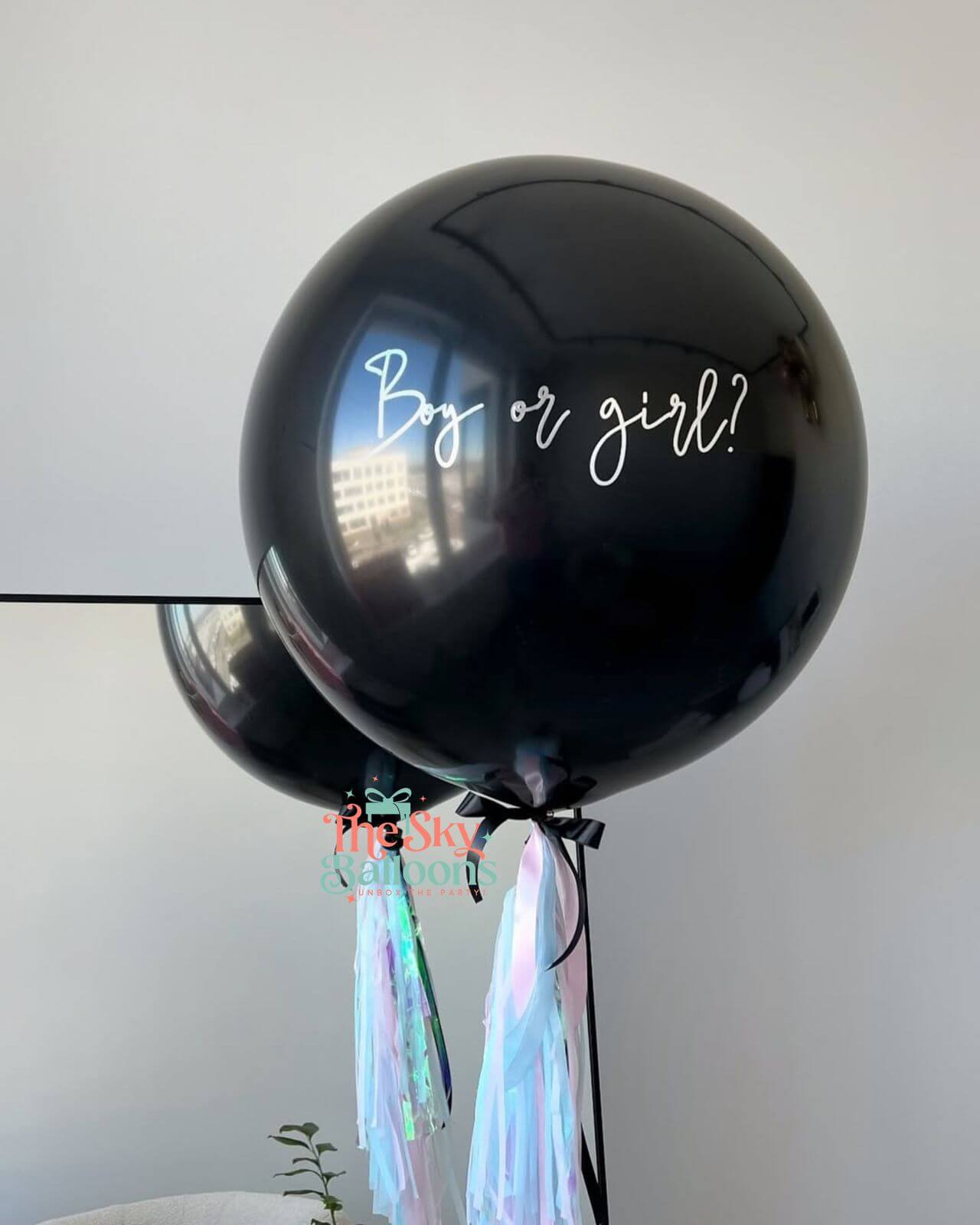 Black balloon with 'Boy or girl?' text and tassels against a light background