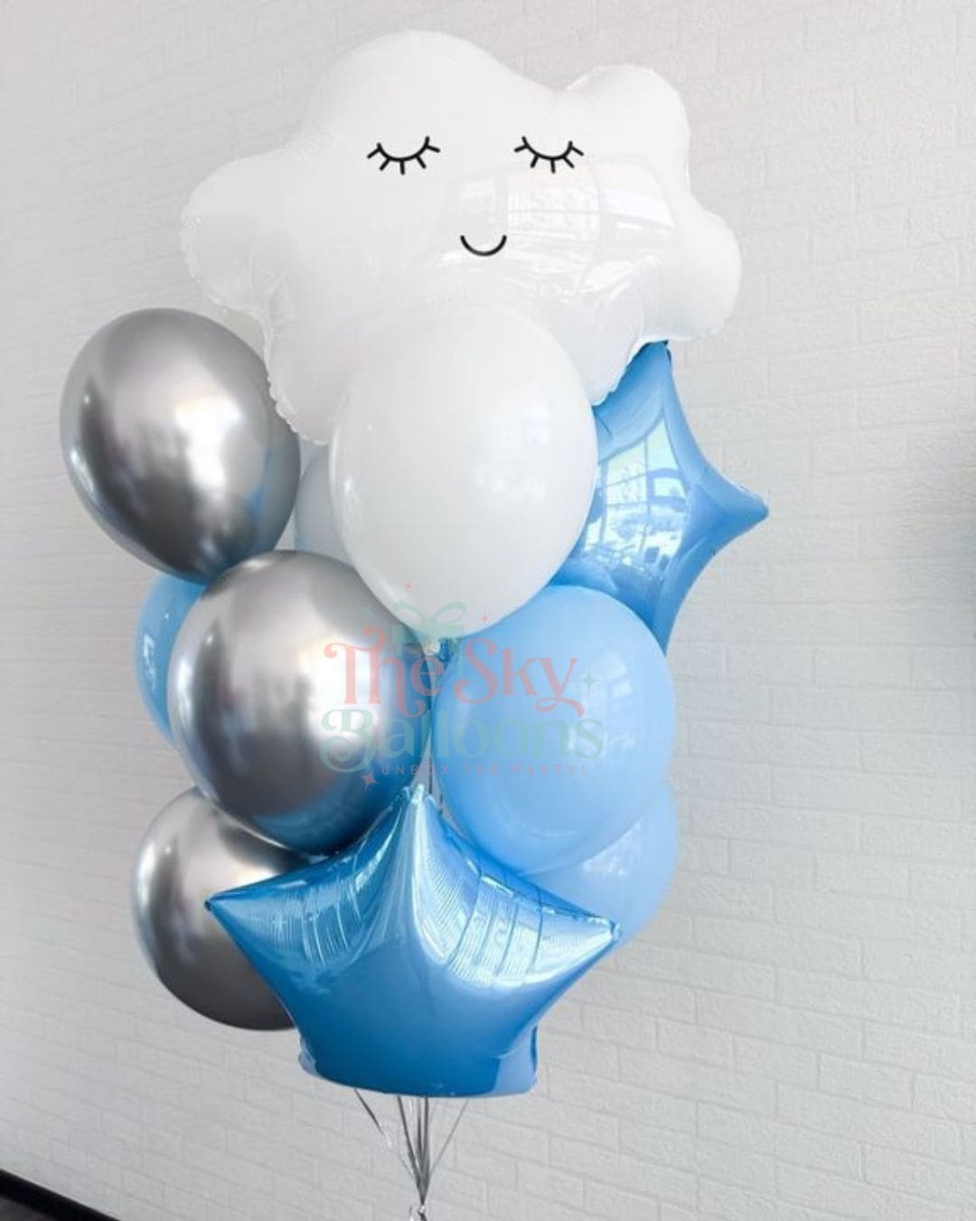 Balloon bouquet with a cloud-shaped balloon and silver and blue balloons against a white brick wall.