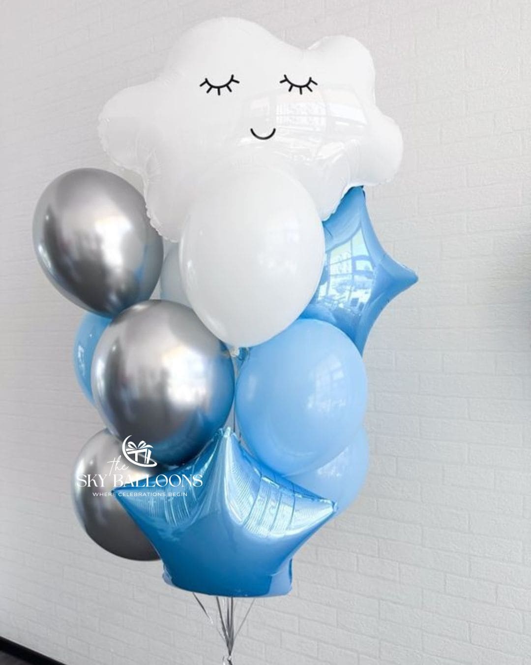Balloon bouquet with a smiling white cloud foil balloon, blue star foil balloons, and light blue, white and metallic silver latex balloons.⠋