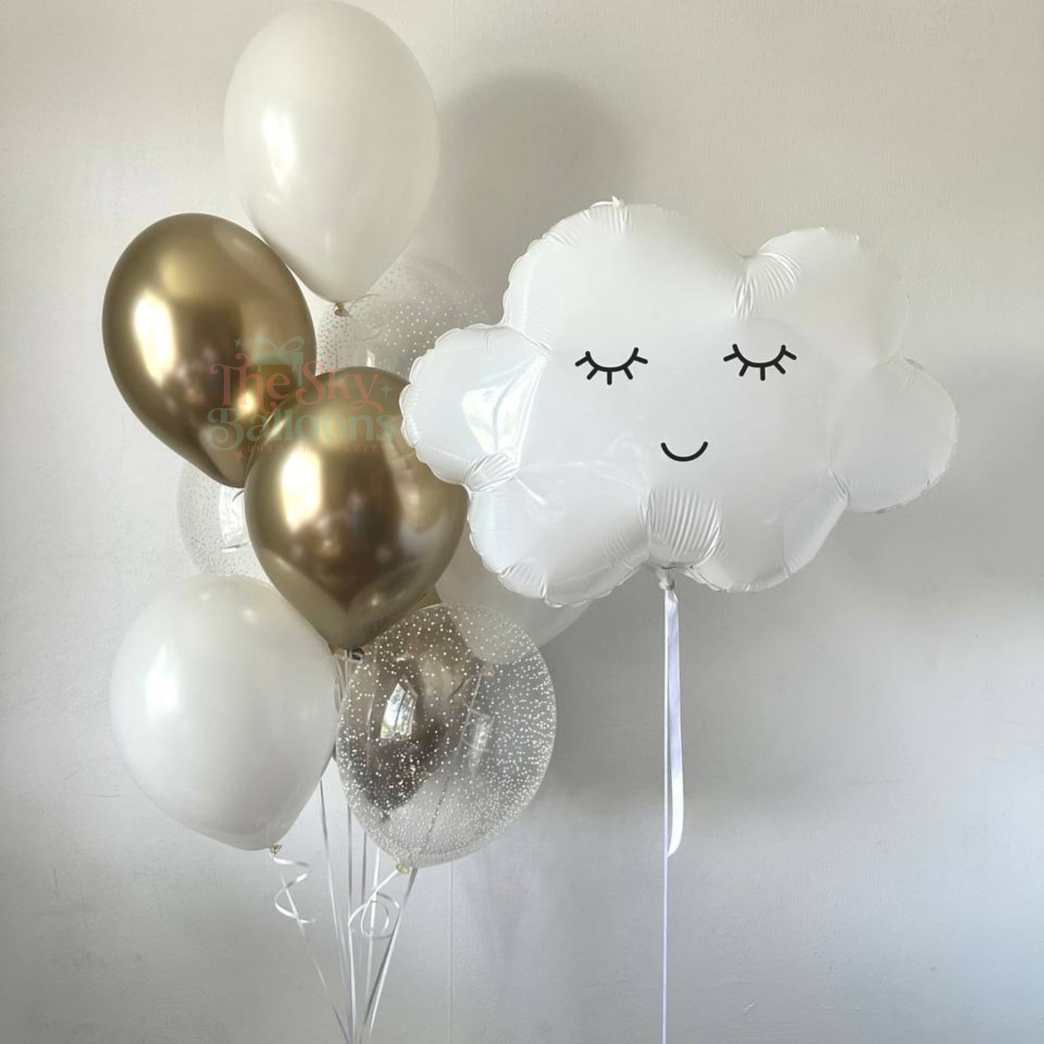 Bouquet of balloons including gold, white, and cloud-shaped balloons on a light background
