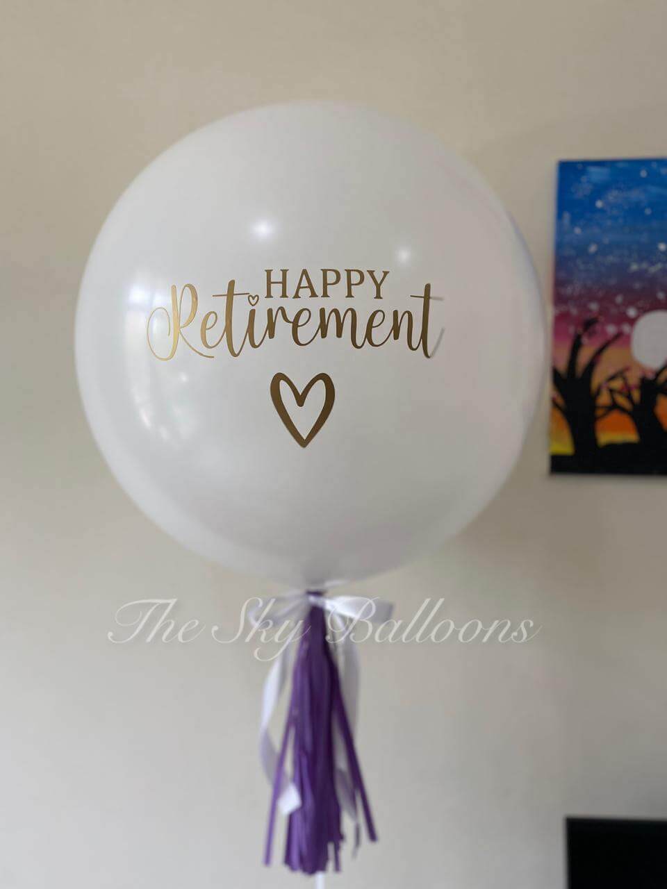 White balloon with 'Happy Retirement' text and heart symbol, featuring a purple tassel, on a plain background.