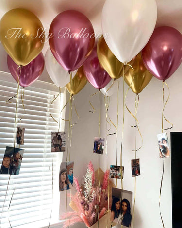 Decorative balloons in gold, pink, and white hanging in a room with photos and a bouquet.