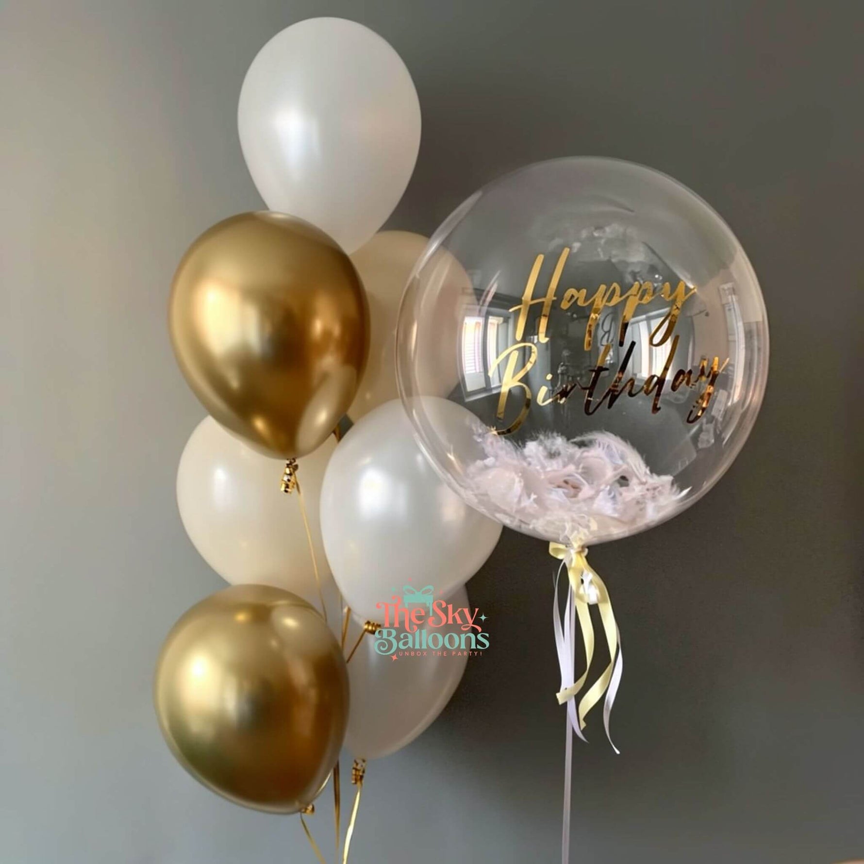 Balloon bouquet with gold, white, and clear balloon featuring 'Happy Birthday' text.
