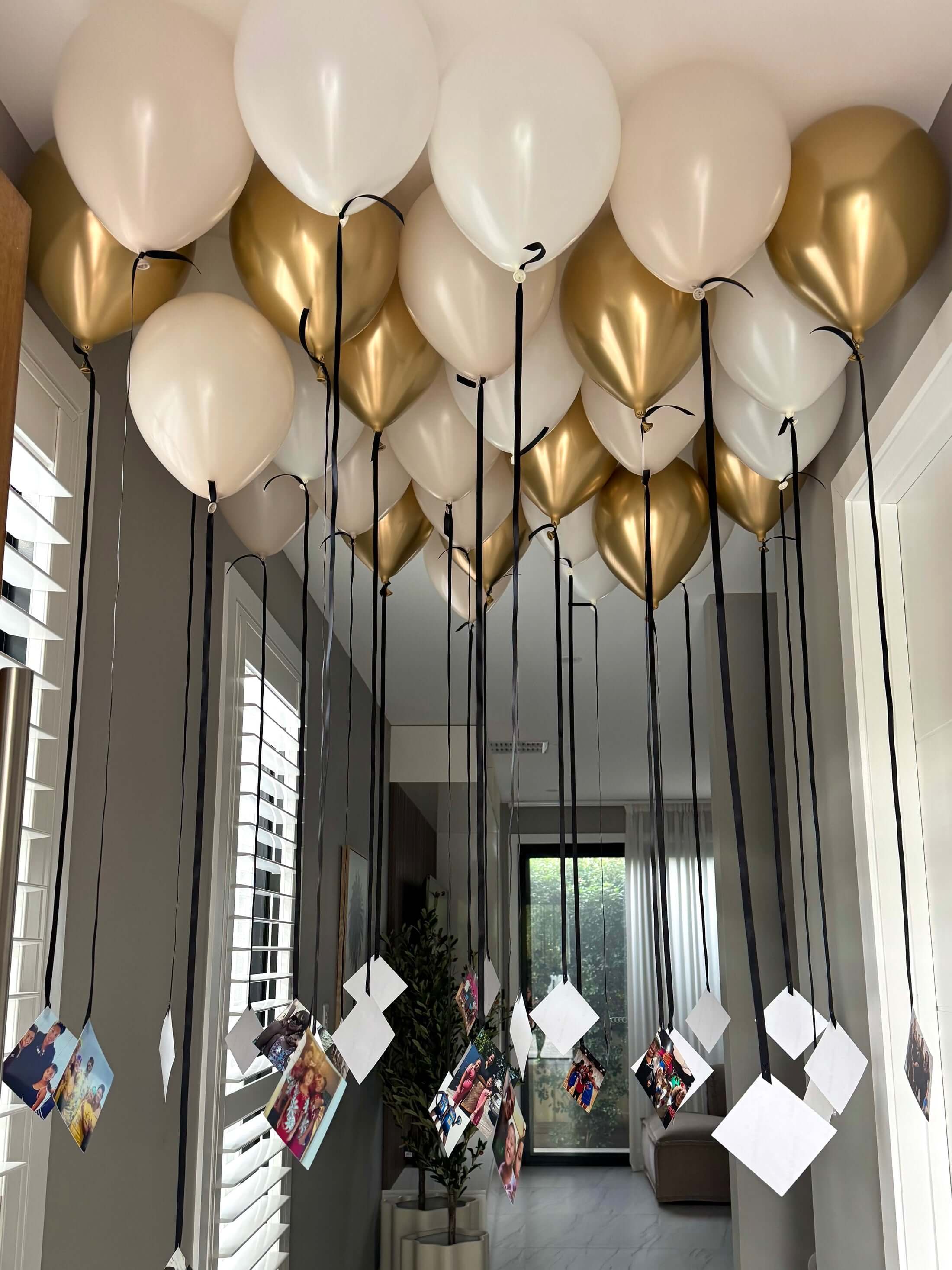 Decorative arrangement of gold and white balloons in a room with large windows.