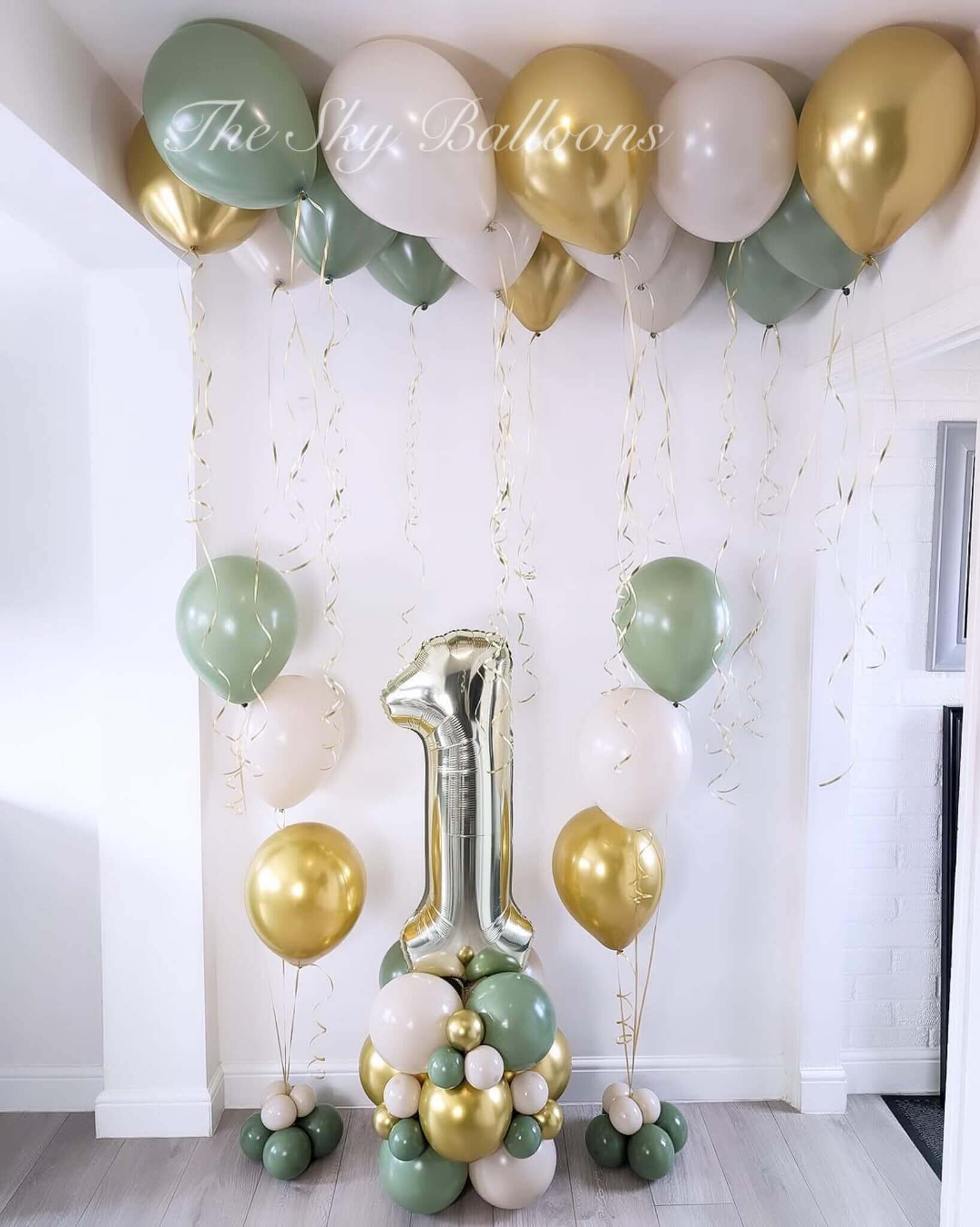 Decorative balloon arch with green, gold, and white balloons in a room.