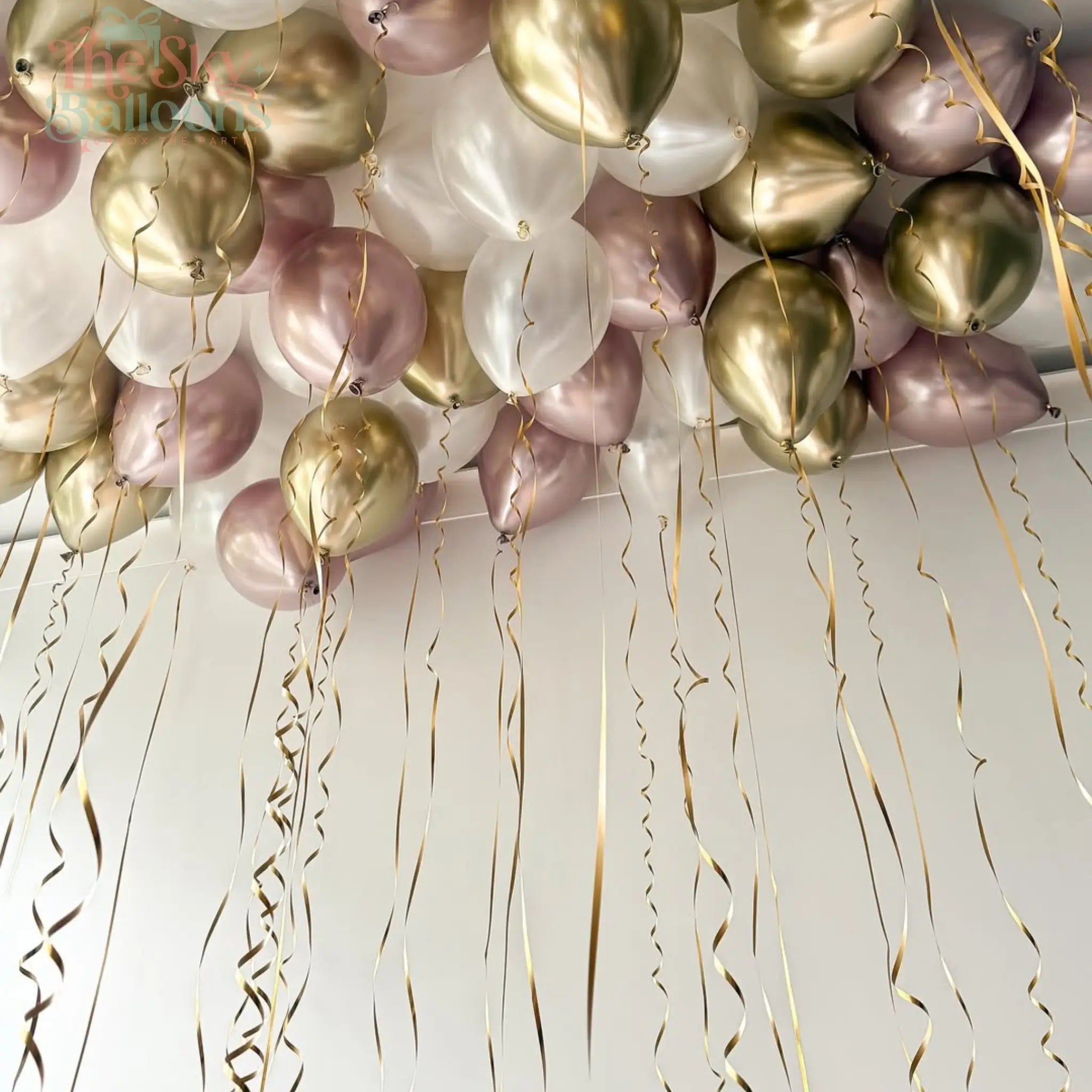 Decorative balloons in gold, pink, and white with streamers on a light background