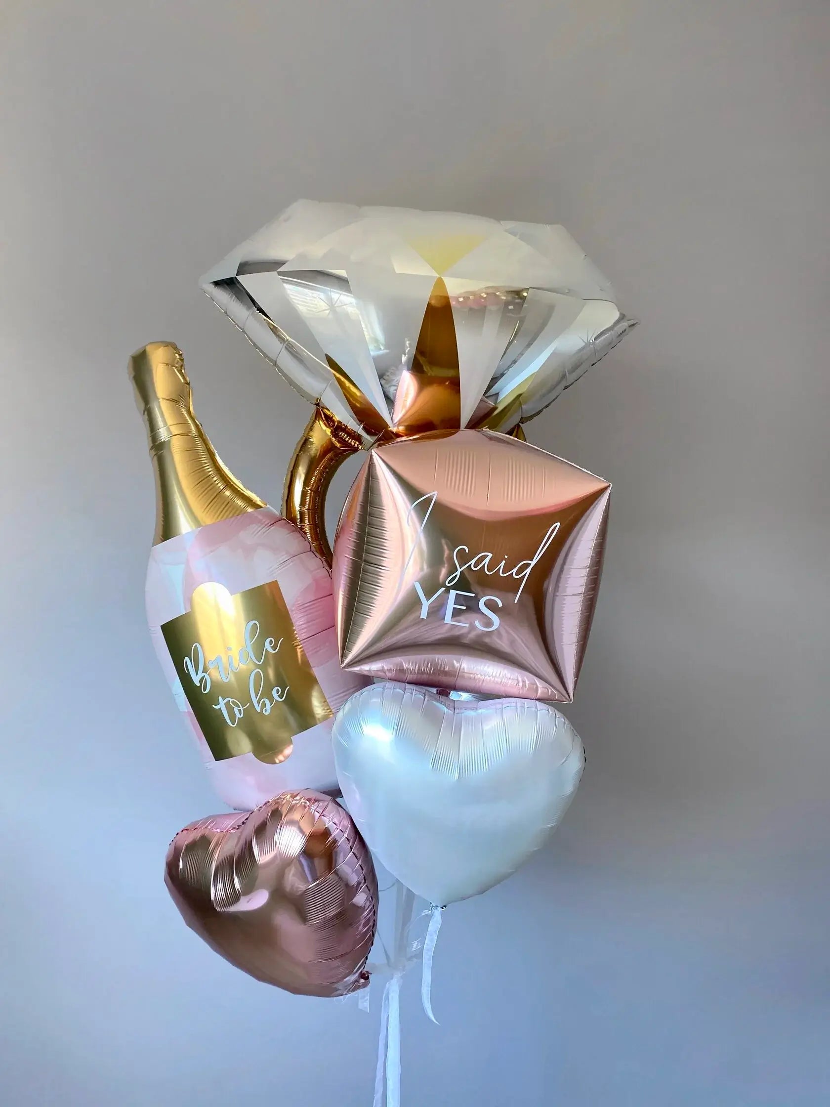 Decorative balloons shaped like a diamond, bottle, and heart with text on a plain background