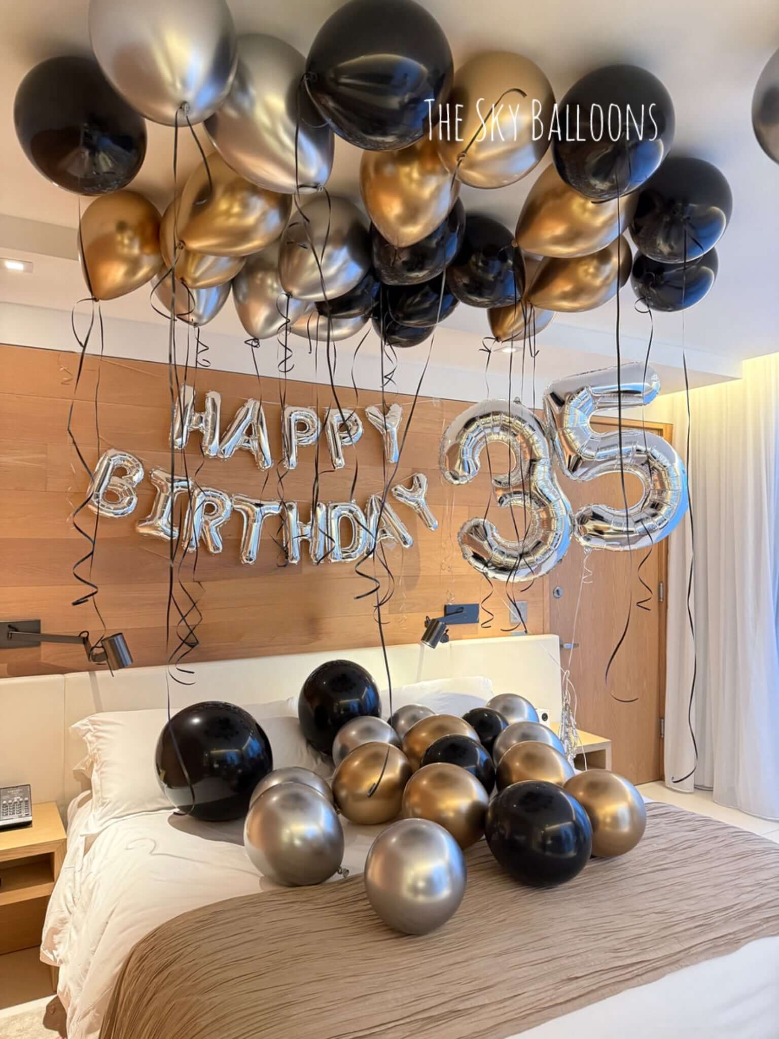 Decorative balloons with 'Happy Birthday 35' on a bed in a room.