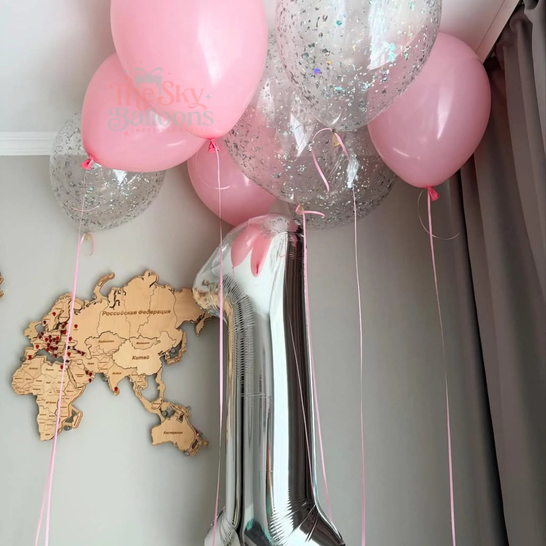 Decorative balloons with ribbons against a neutral wall with a world map.