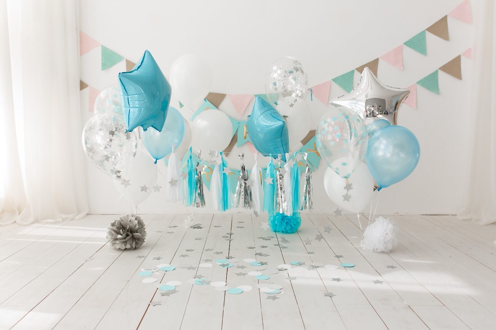 Decorative setup with balloons and streamers on a white floor and wall.