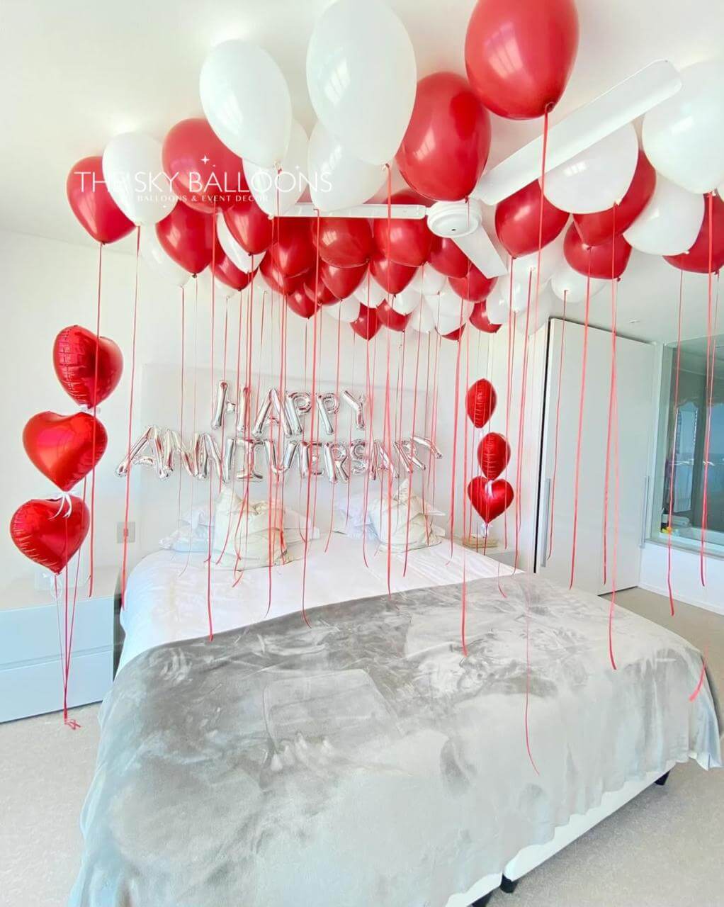 Decorative setup with red and white balloons and 'Happy Anniversary' text in a bedroom.