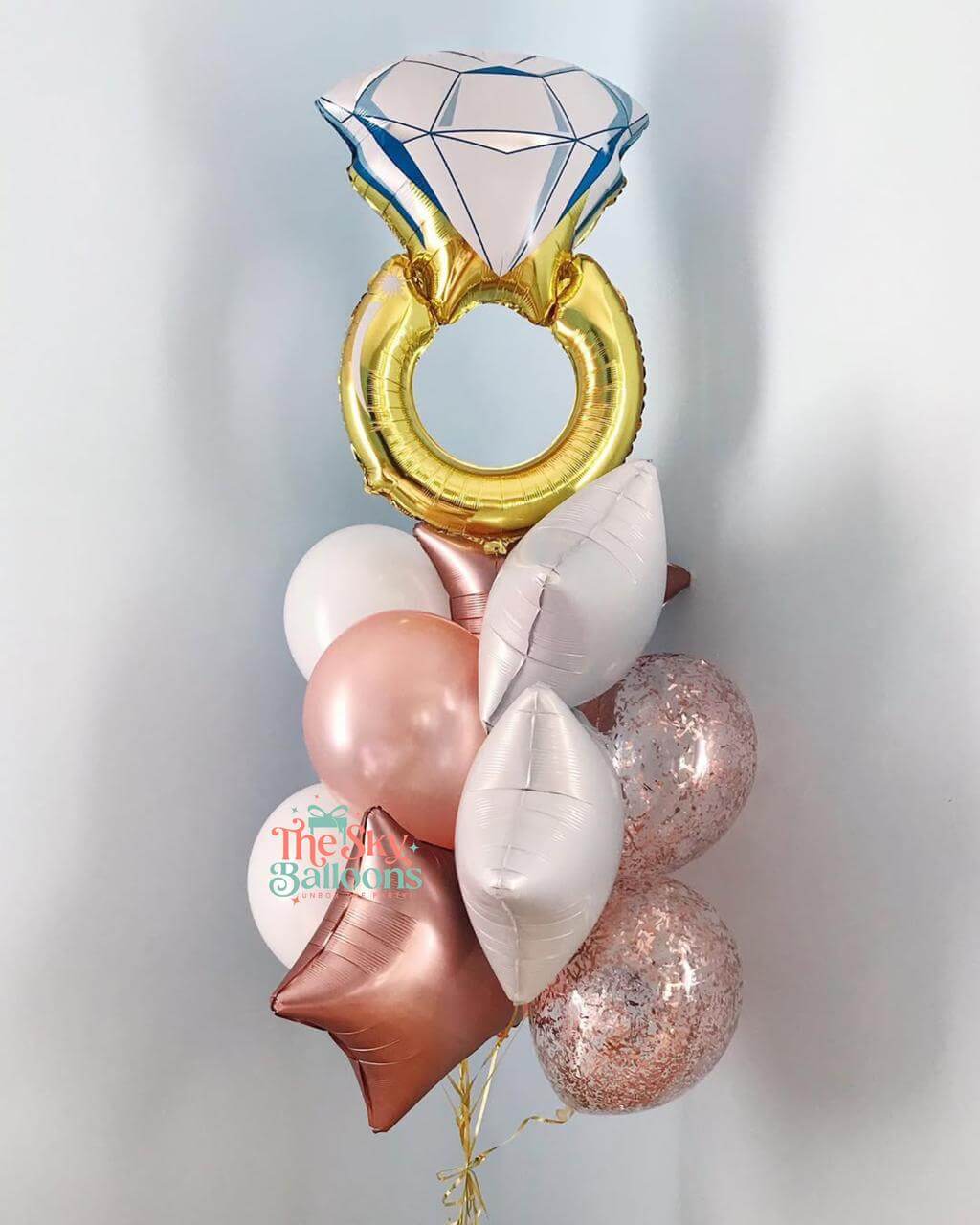 Balloon bouquet with diamond ring and heart shapes on a light gray background