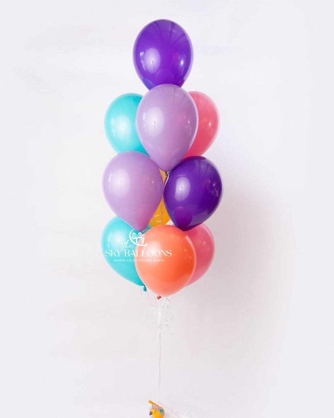A cluster of latex balloons in purple, teal, lavender, pink, and orange, tied together with a clear string against a plain white background.