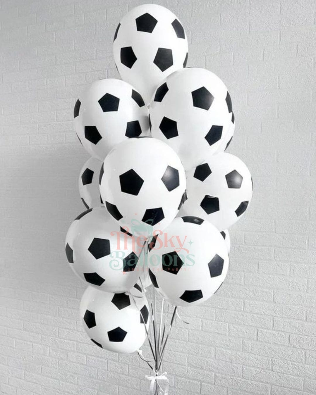 Bunch of soccer ball-shaped balloons against a light gray brick wall.