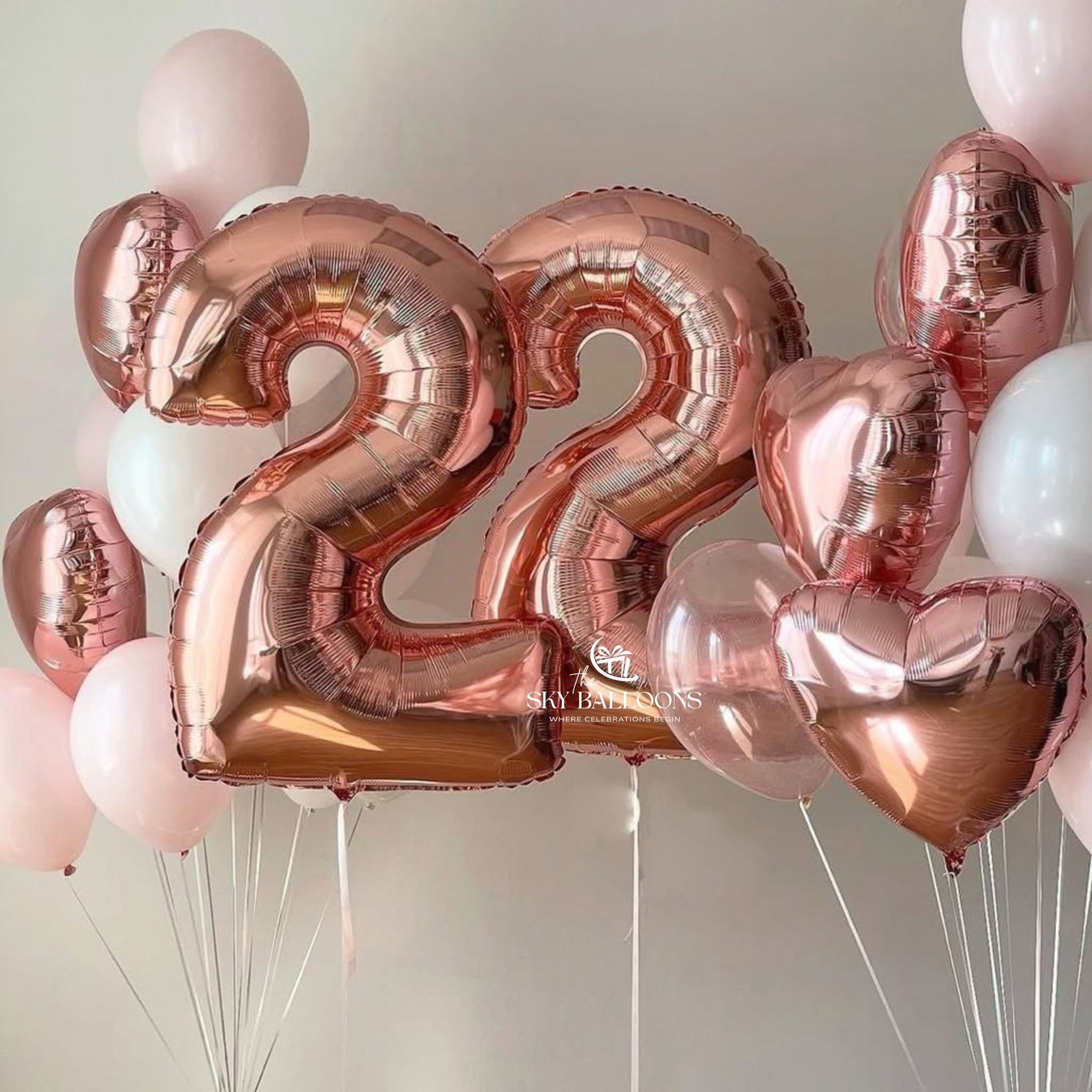 Rose gold foil number 22 balloons and matching pink, white, and rose gold heart balloons arranged together against a plain light background. 