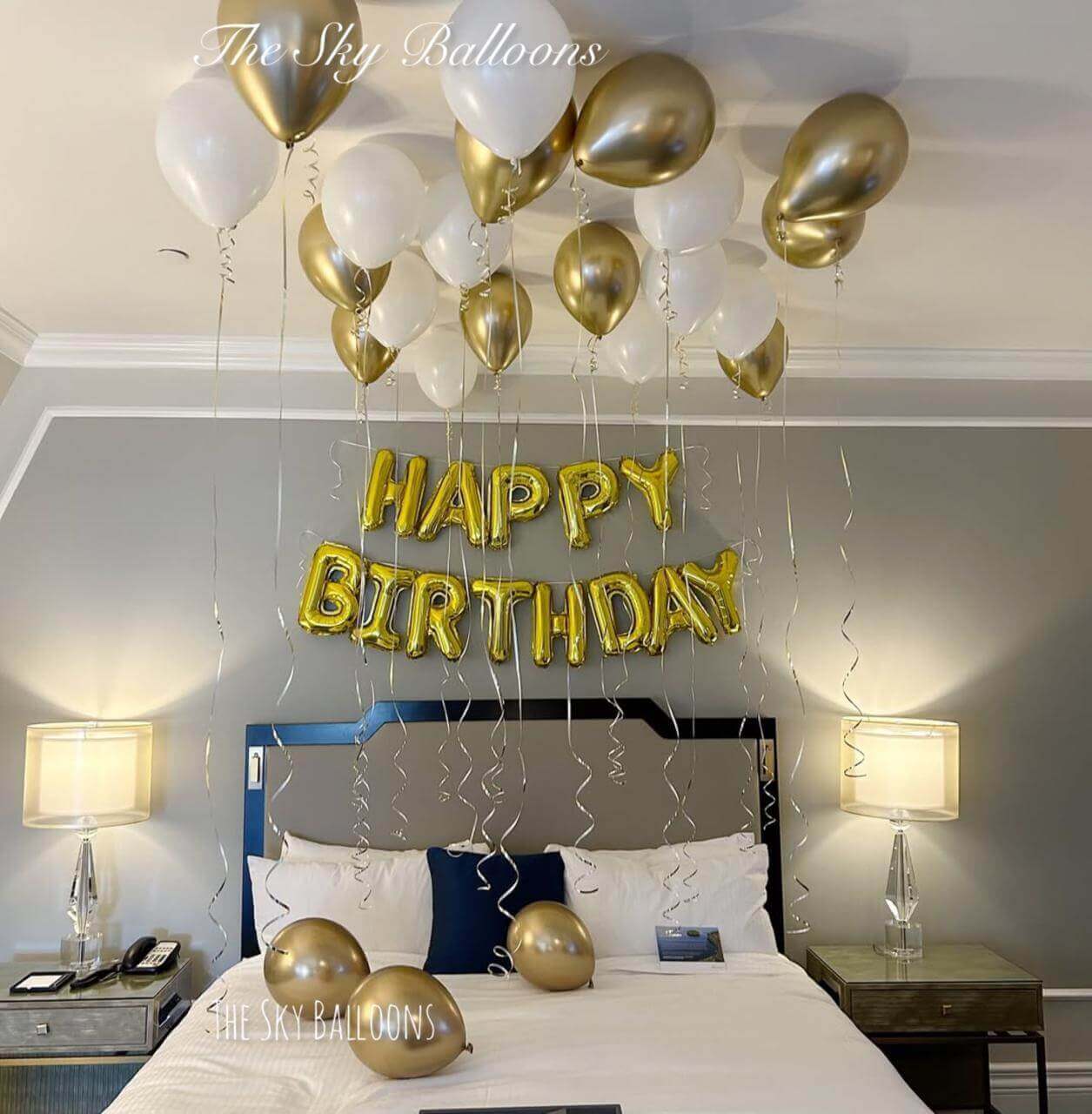 Gold Happy Birthday letter balloons with white and gold ceiling balloon display in elegant bedroom setting