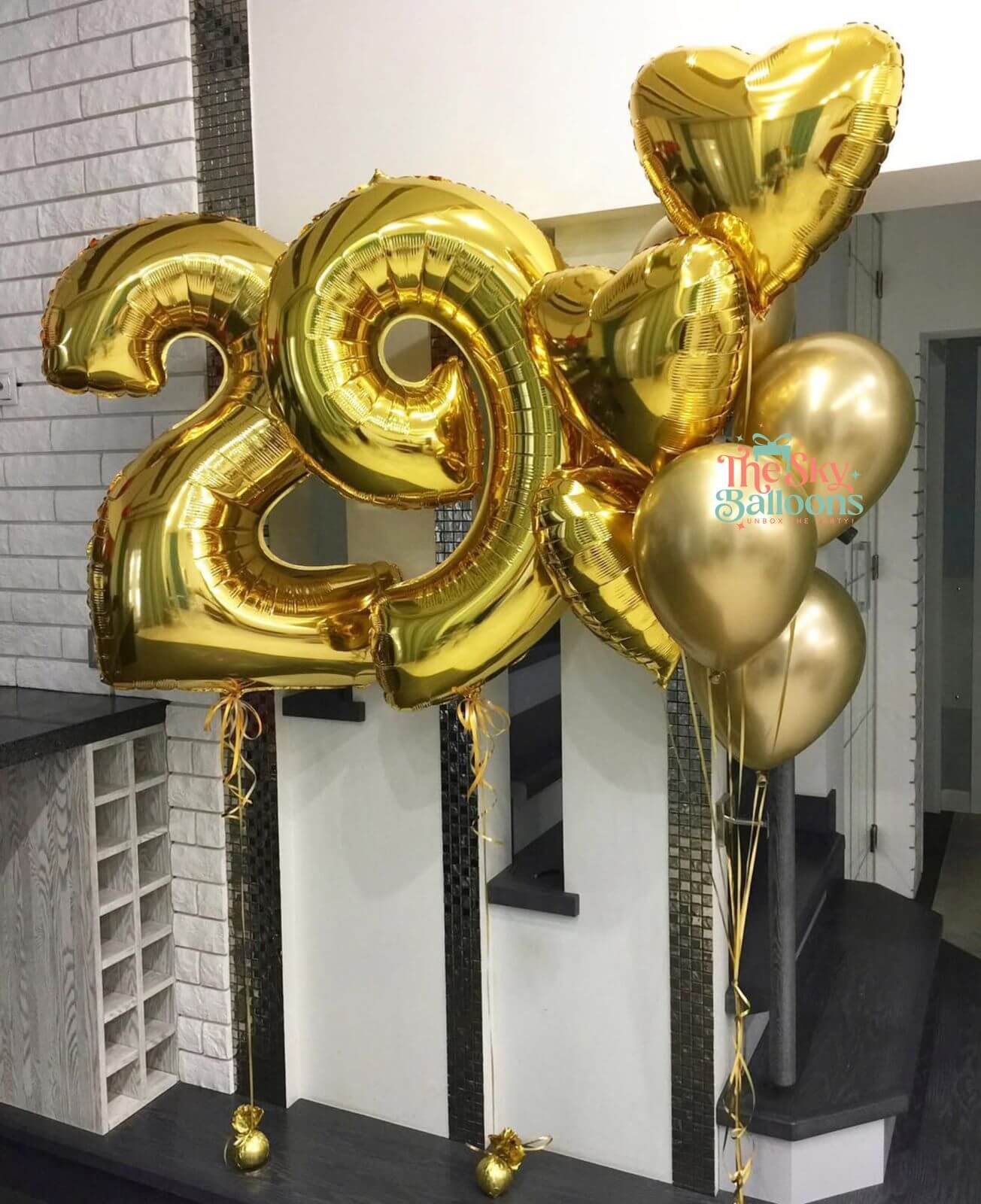 Gold number 29 balloon with additional gold balloons against a white wall.