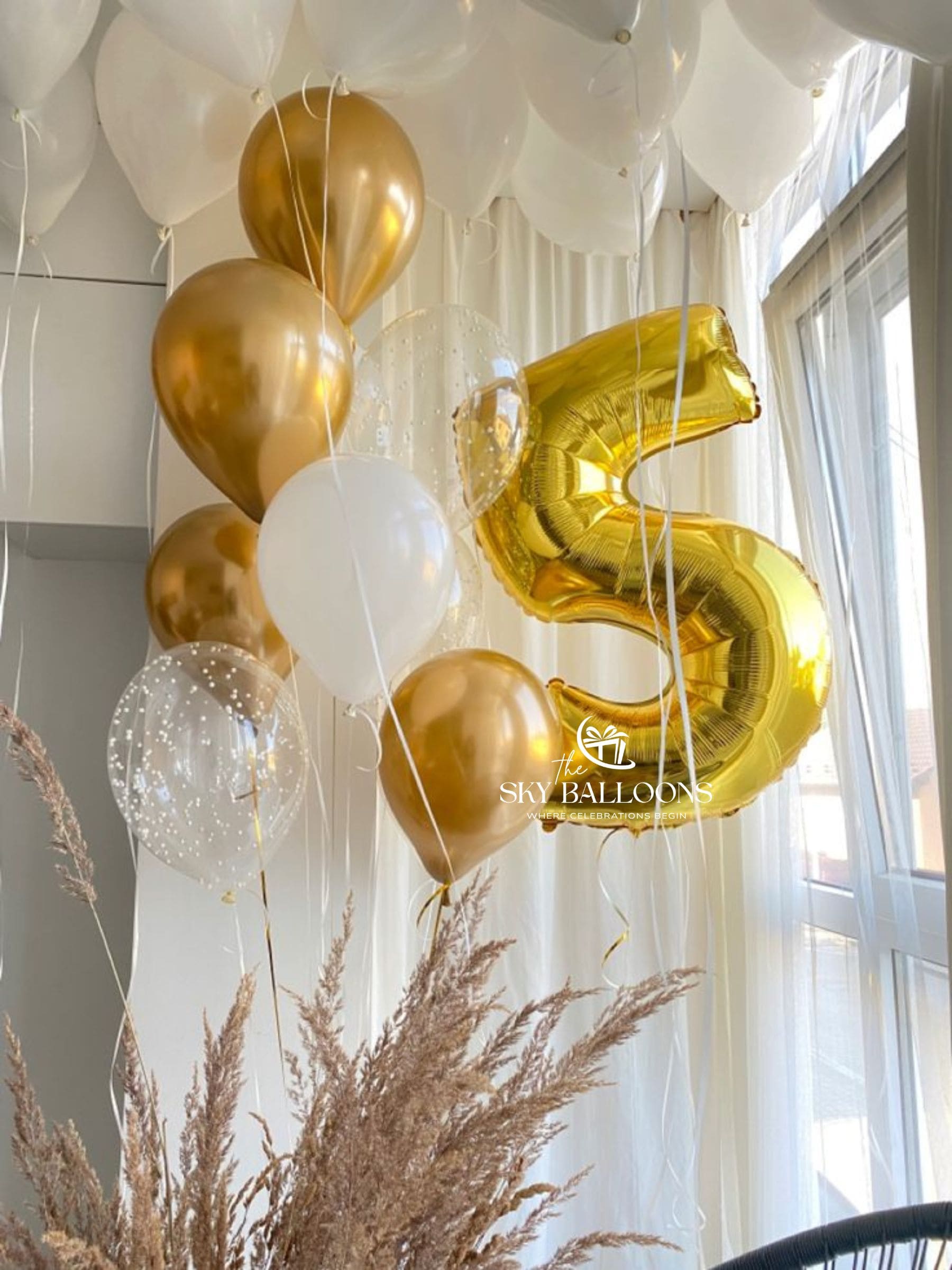 Gold number 5 foil balloon with a gold, white and clear confetti balloon bouquet beneath white ceiling balloons.