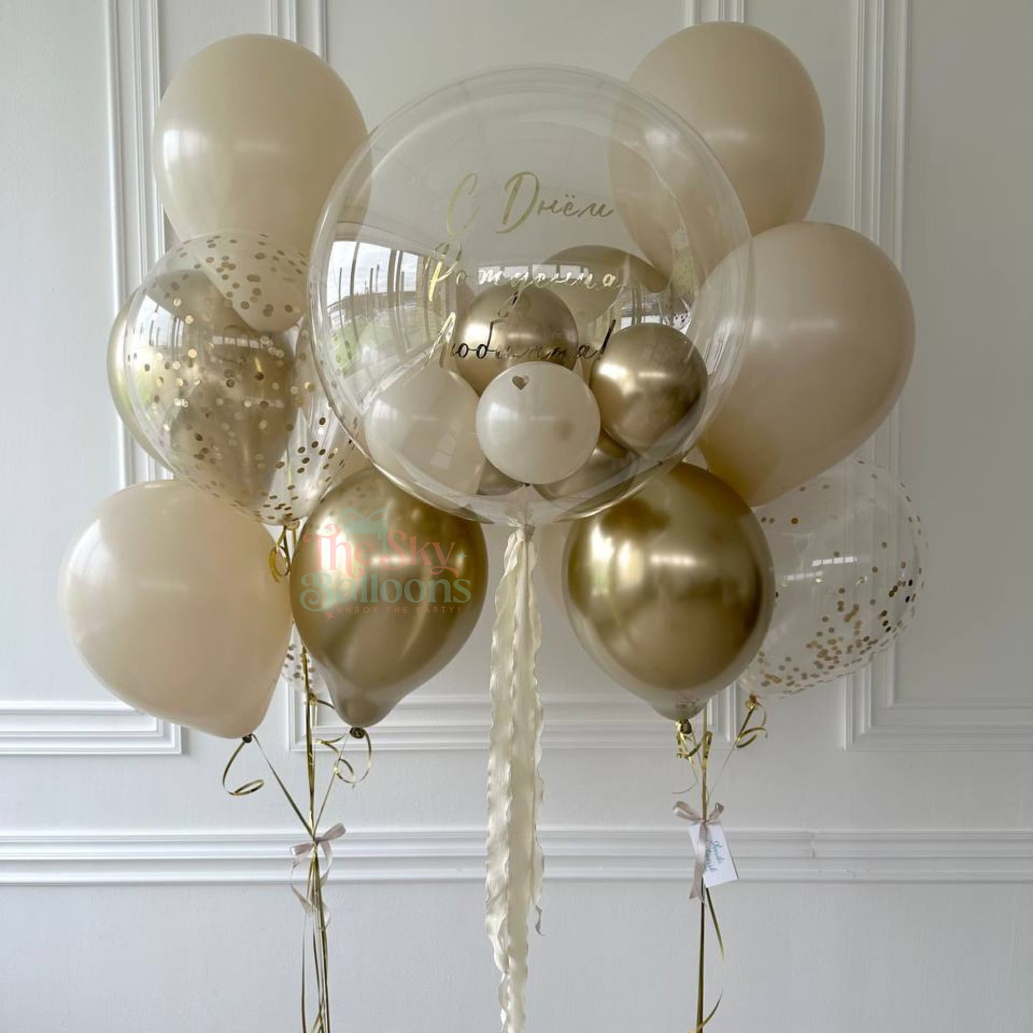 Decorative balloons with gold, beige, and clear balloons against a white wall.
