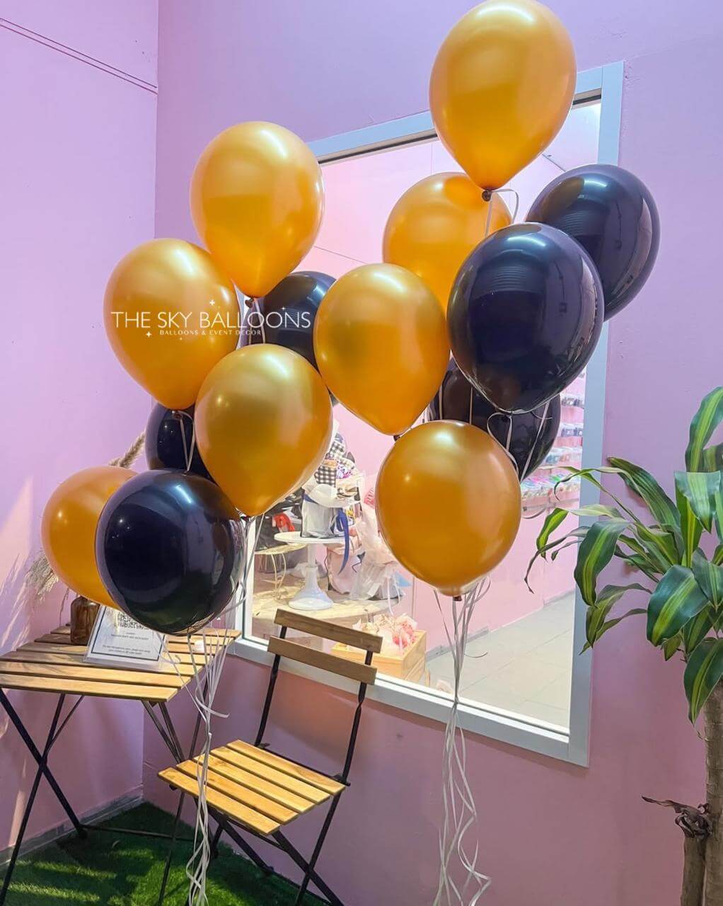 Gold and black balloons with 'The Sky Balloons' branding against a pink wall.