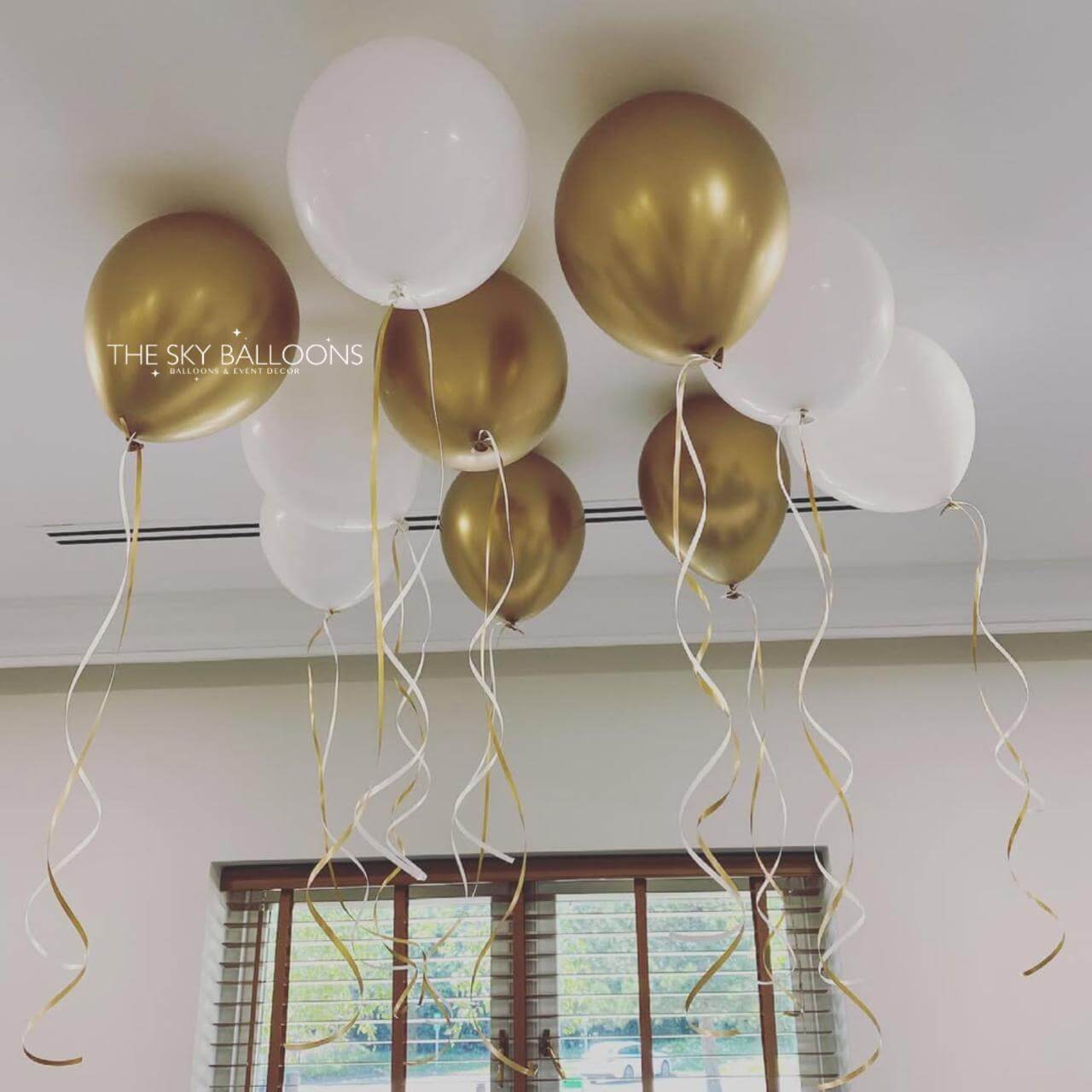 Gold and white balloons with ribbons hanging from a ceiling