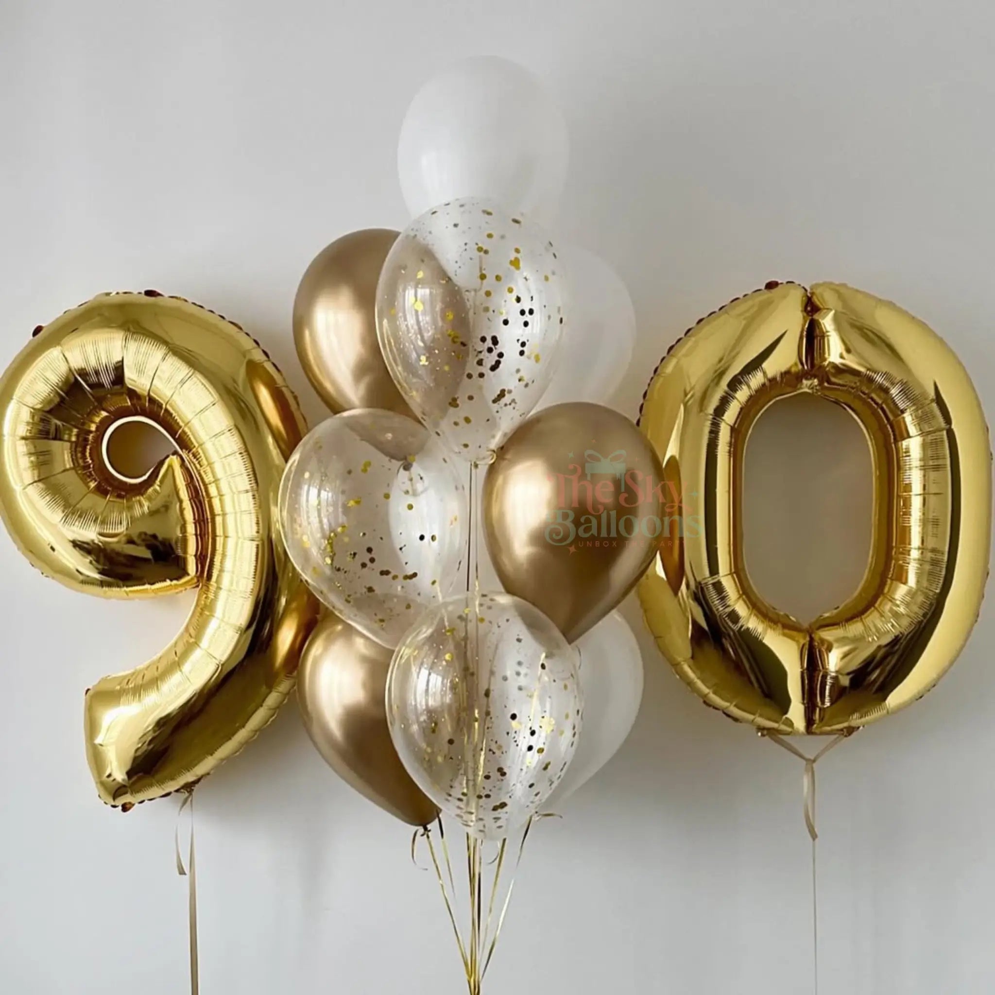 Gold and white balloons shaped like numbers '9' and '0' on a light gray background.