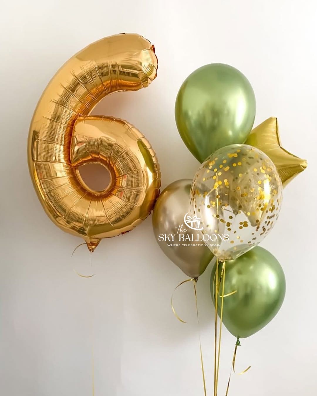 A balloon bouquet featuring a large metallic gold foil number 6 balloon, three metallic sage green latex balloons, a clear latex balloon filled with gold confetti, and a small metallic gold star balloon, set against a plain off-white background.