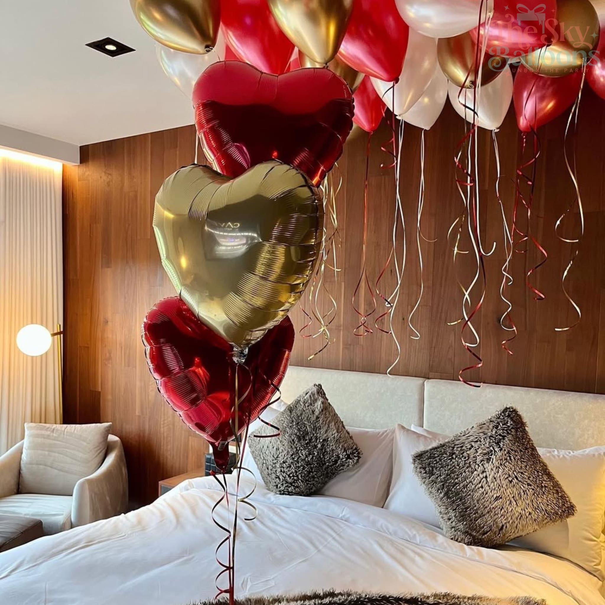 Heart-shaped balloons in red, gold, and white above a bed in a bedroom.
