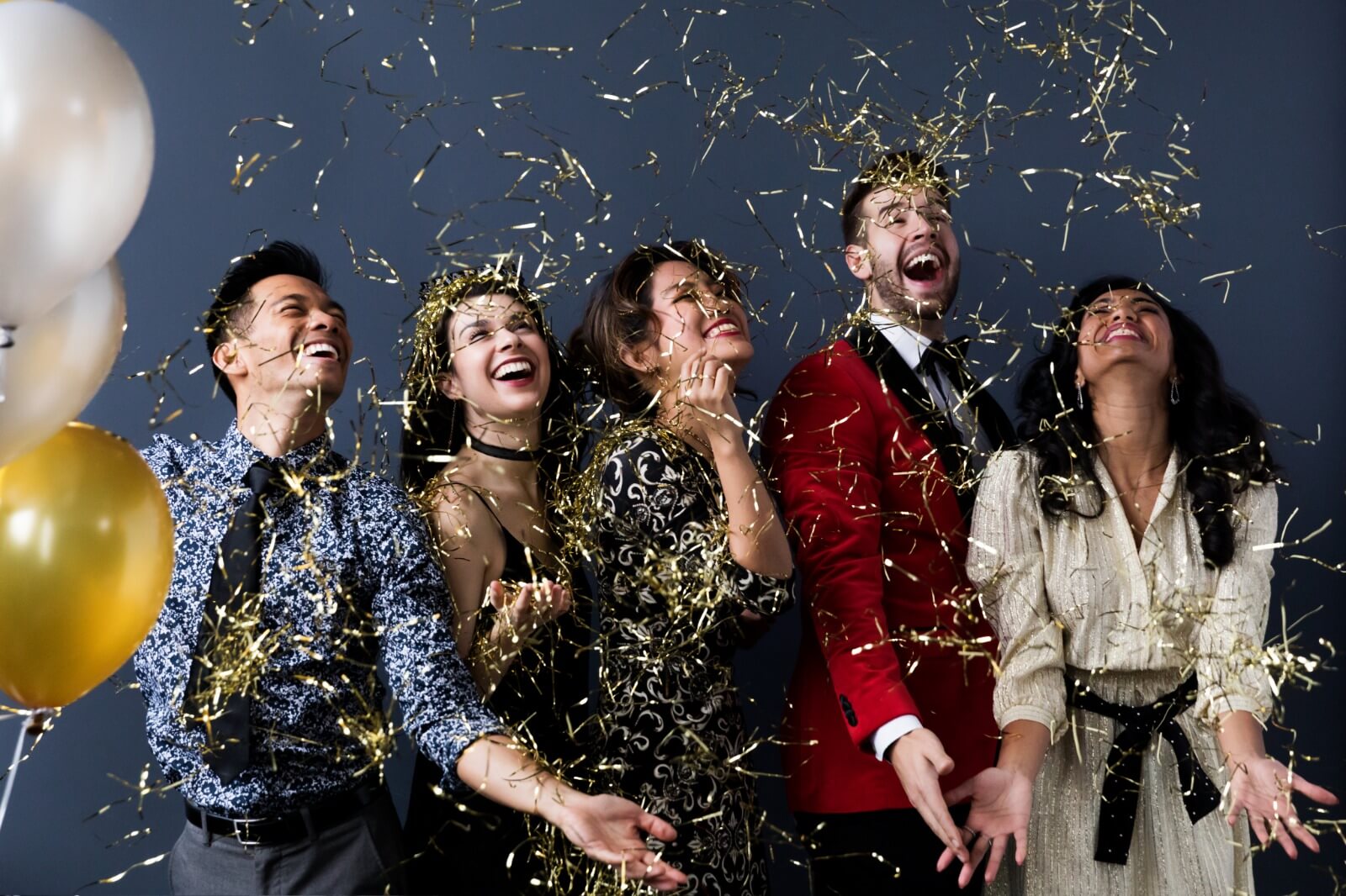 Group of people celebrating with confetti and balloons against a dark background