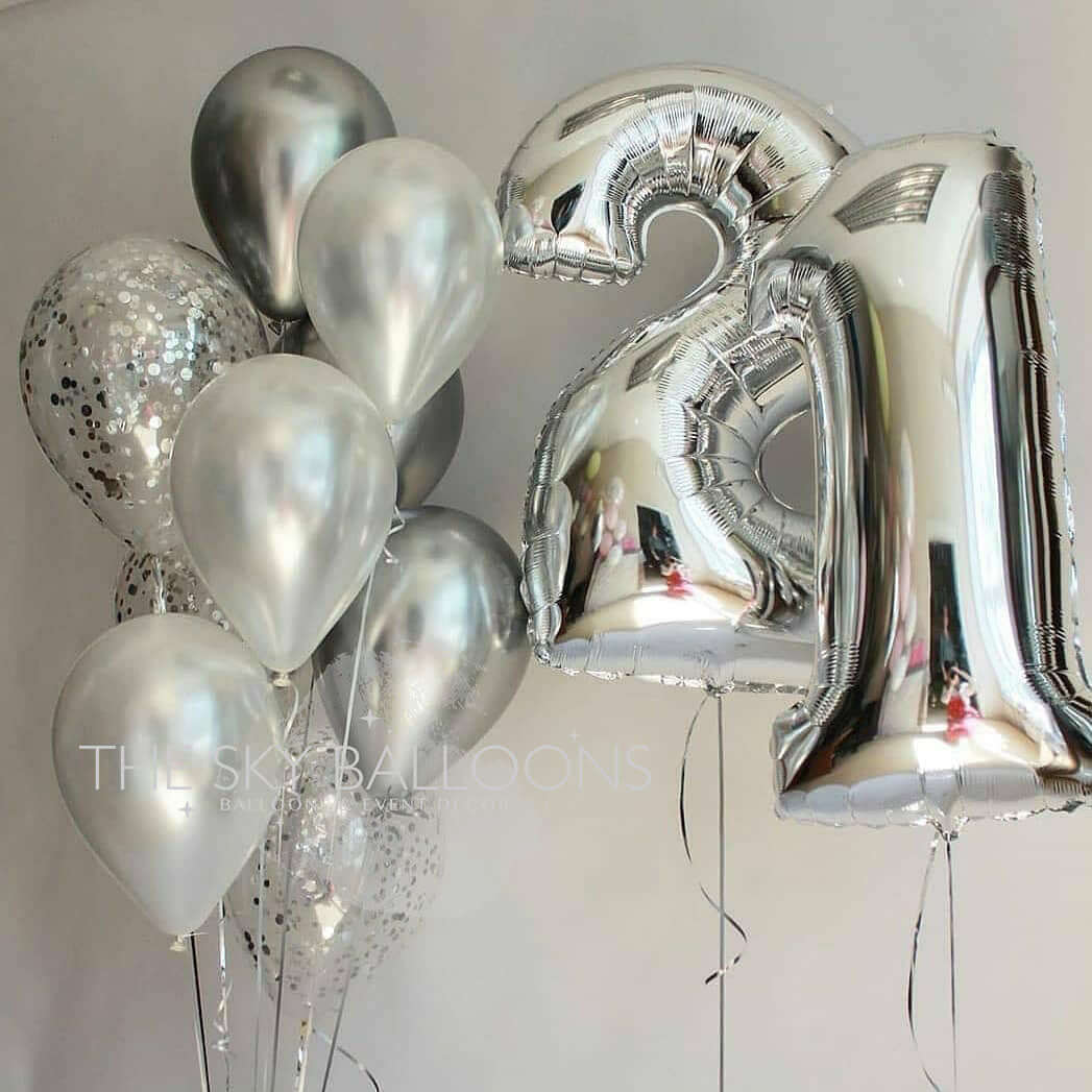 A bouquet of balloons including silver latex, helium-filled balloons with a large '21' foil balloon, and confetti balloons.