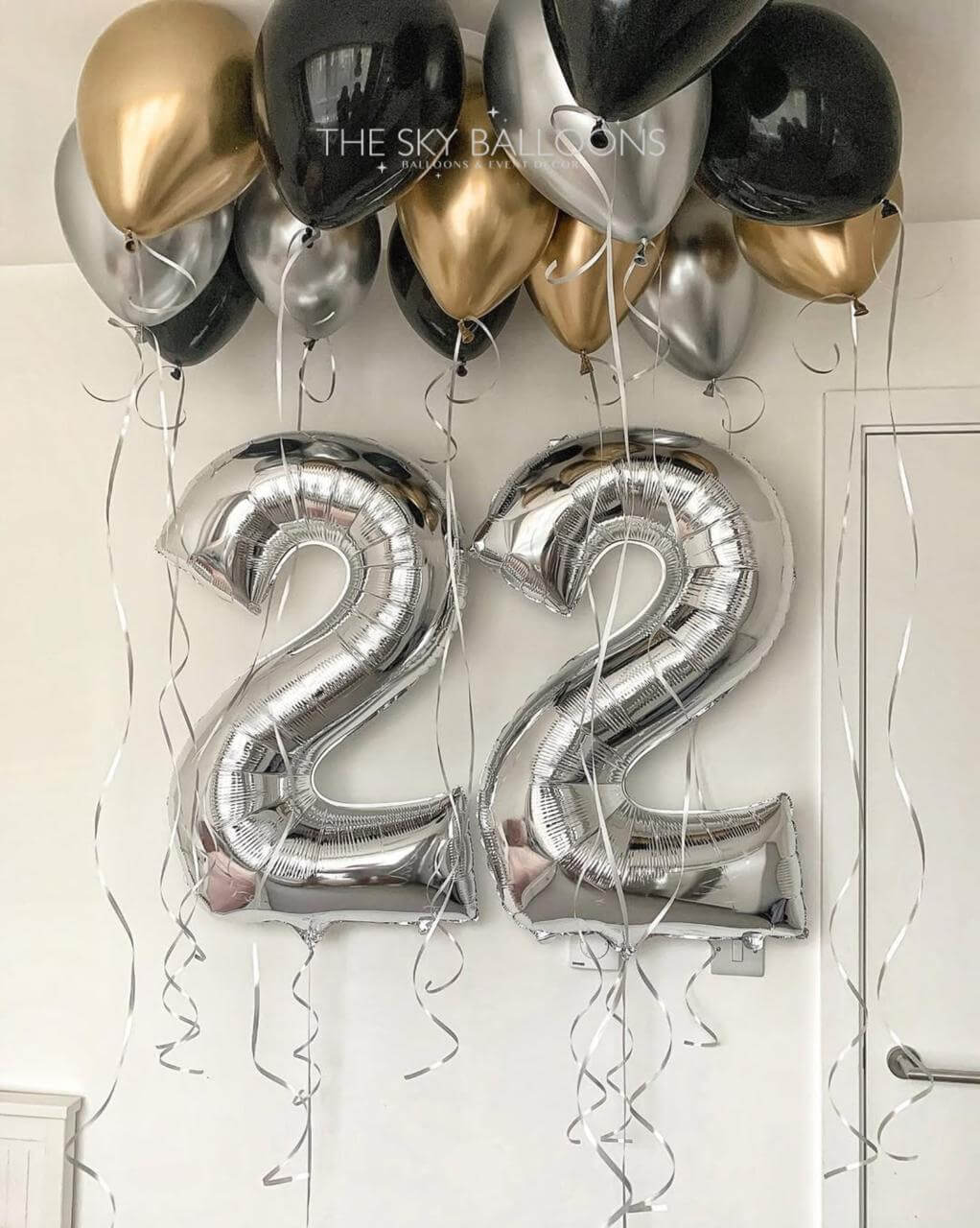 Silver number '22' balloons with gold, black, and silver balloons against a white wall.