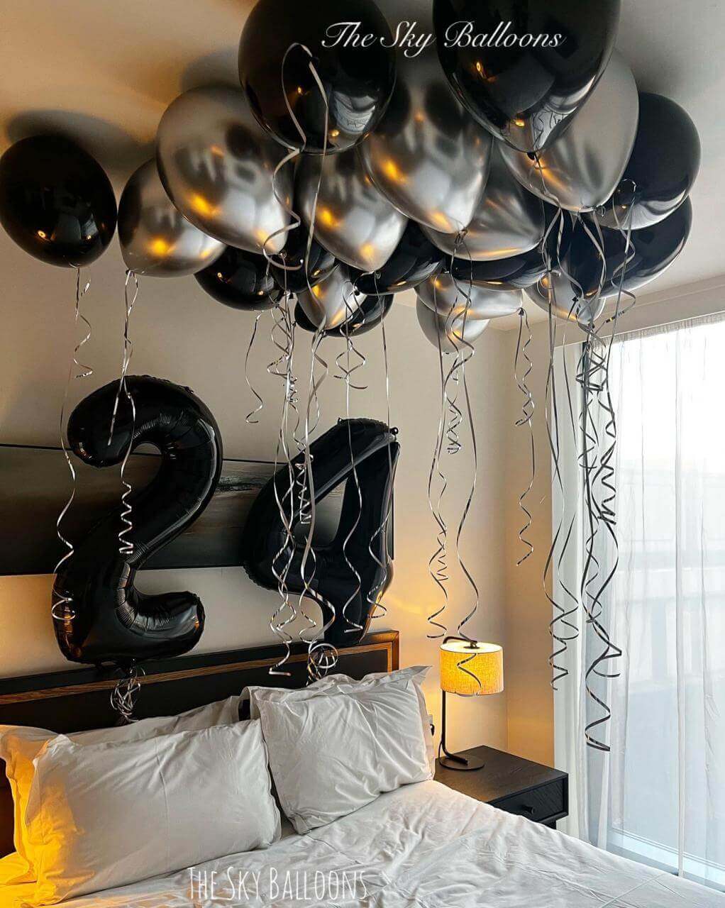 Happy 24th birthday balloon arrangement featuring black and silver balloons in an elegant party setup