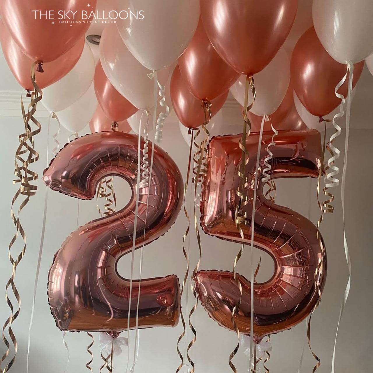 Rose gold number '25' balloons with pink and white balloons against a neutral background