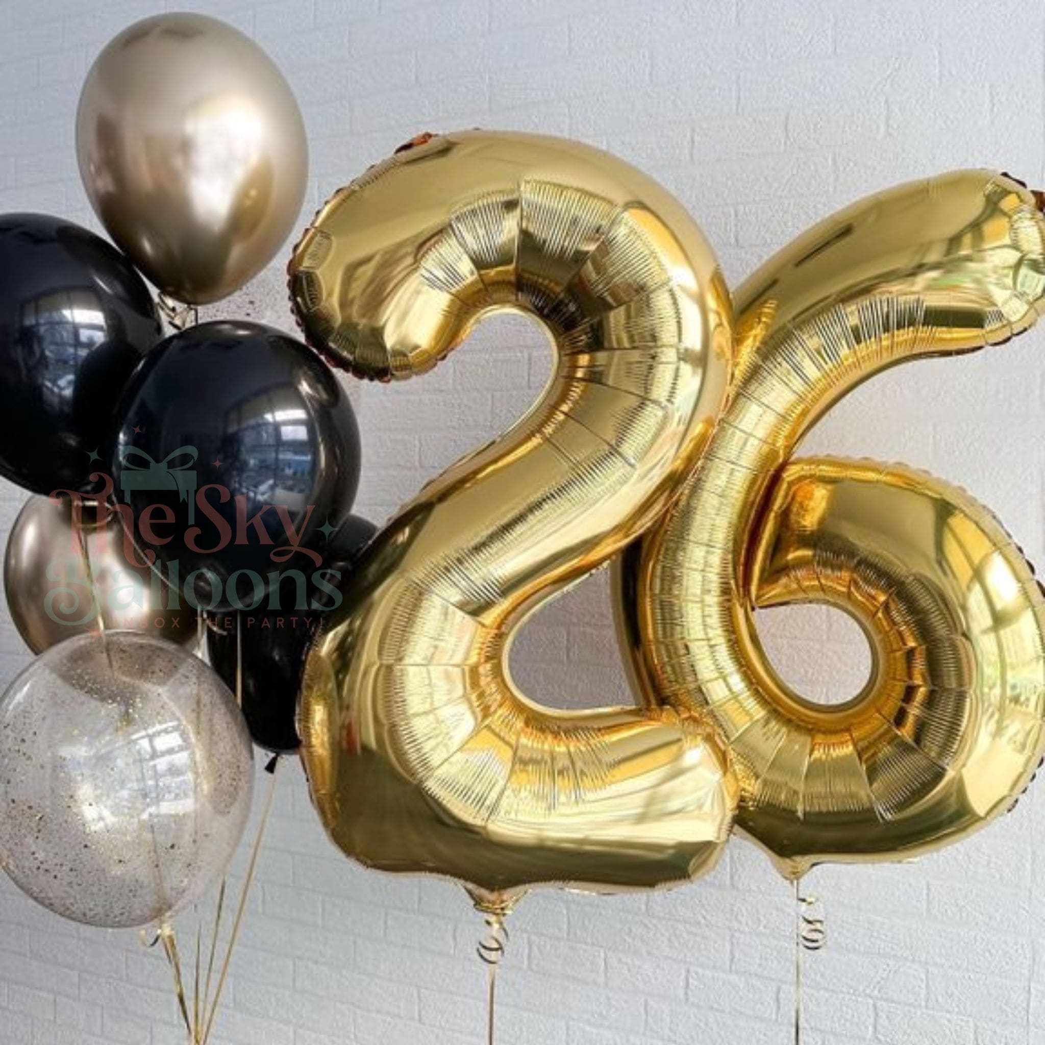 Gold number 26 balloon with other balloons against a white brick wall background