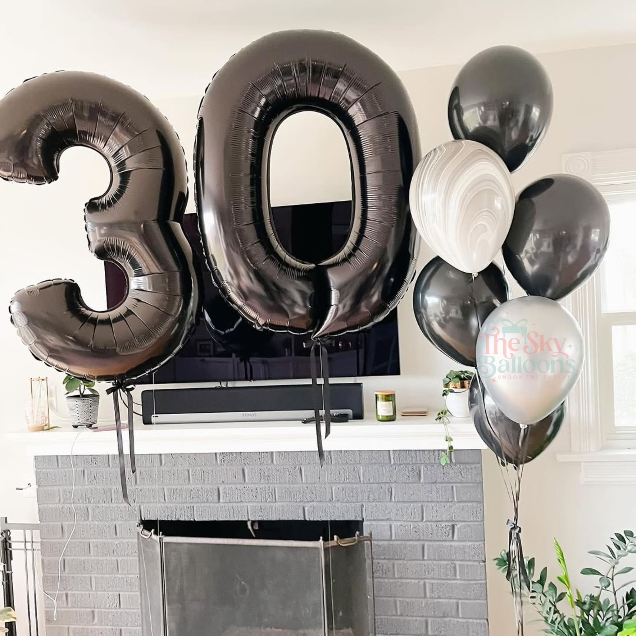Black and white balloons with '30' and 'The Sky is the Limit' text in a room with a fireplace.
