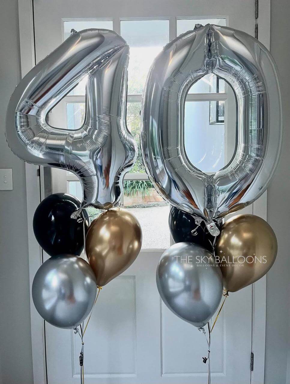 Silver number '40' balloons with smaller gold, black, and silver balloons against a white door background.