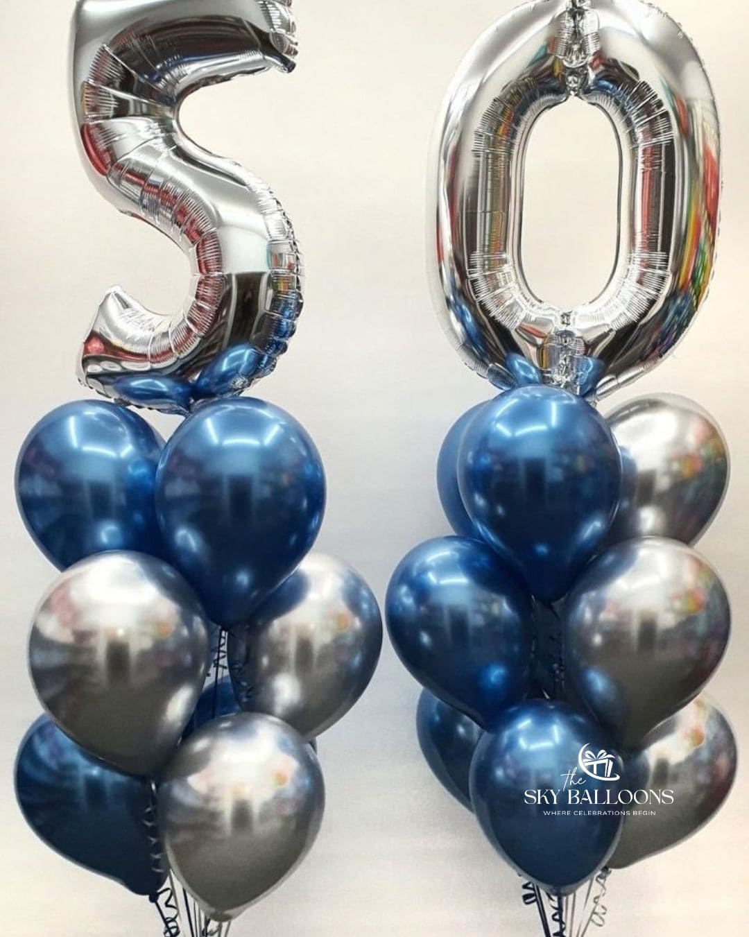 Silver number 50 foil balloons above two matching bouquets of metallic navy blue and silver latex balloons with curling ribbons.