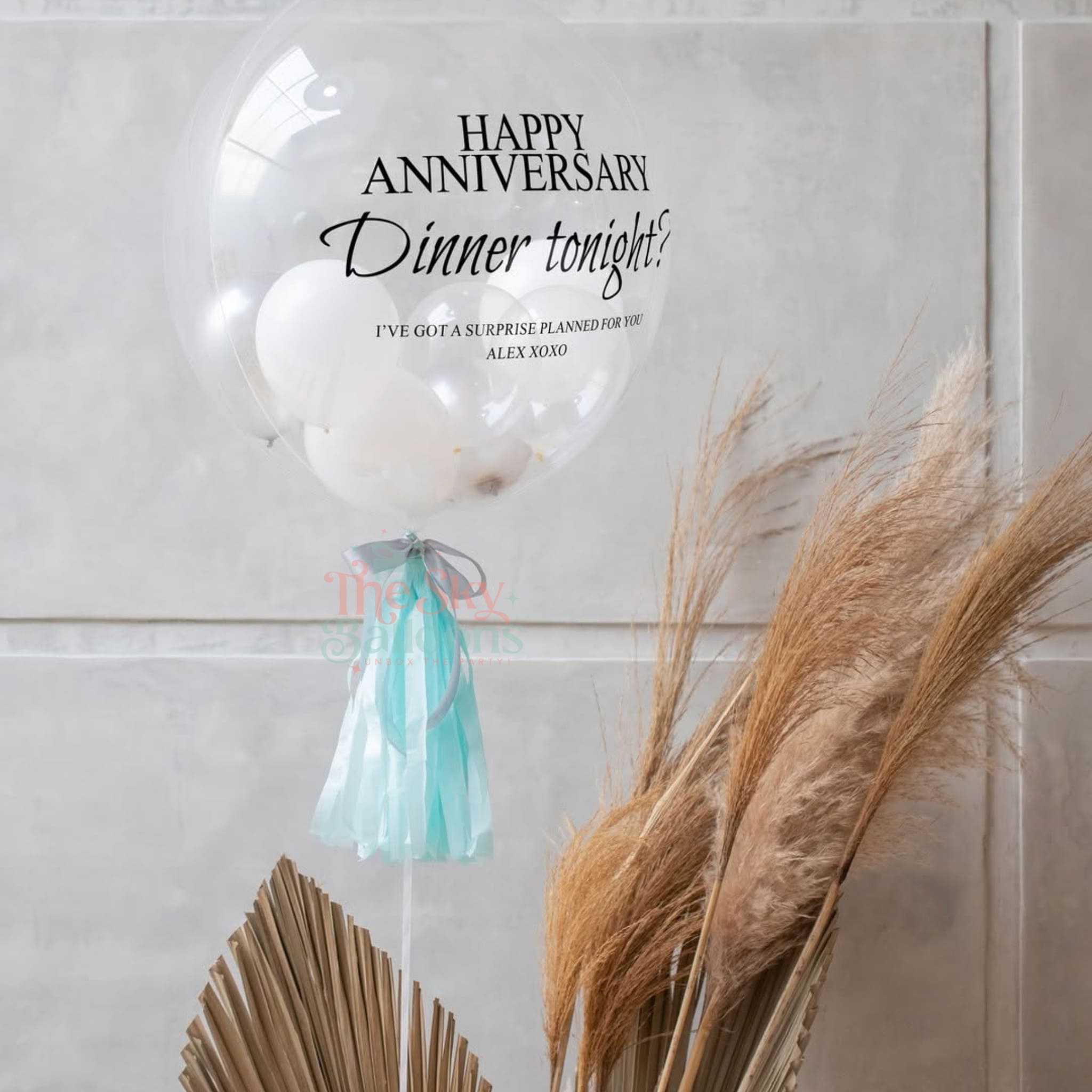 Decorative balloon with 'Happy Anniversary Dinner tonight!' text on a light background with pampas grass.