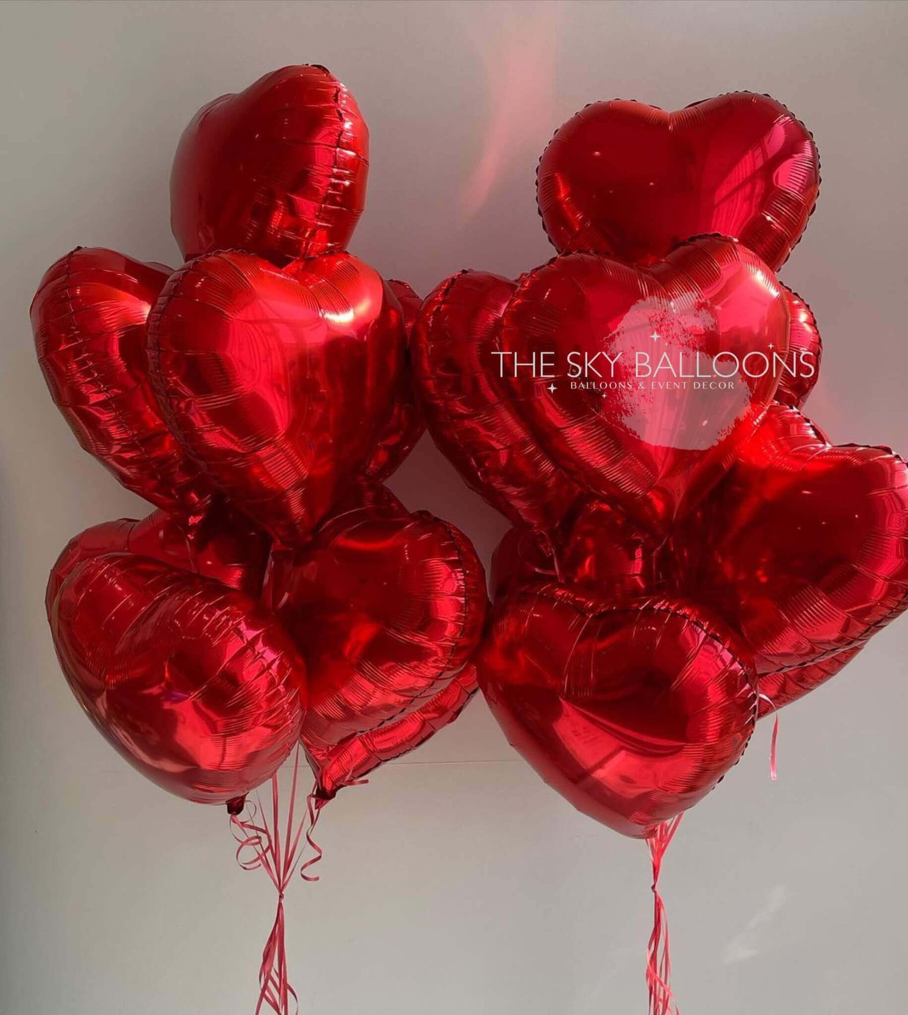 A bunch of inflated red heart-shaped foil balloons with the text 'THE SKY BALLOONS' on a reflective surface.