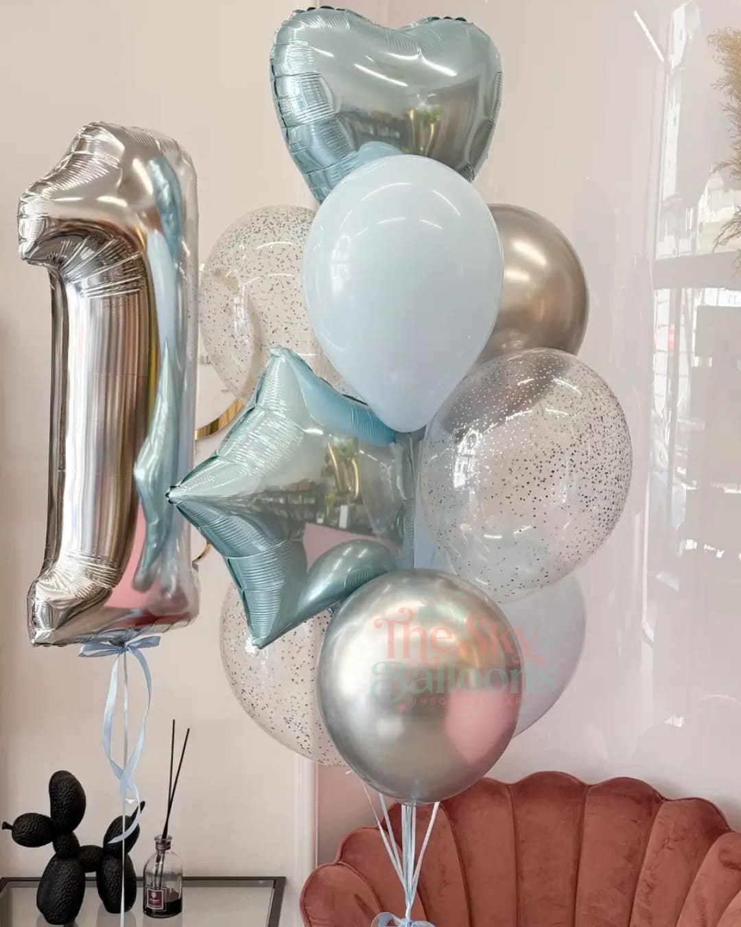 Bouquet of balloons including a large silver number '1' and various other shapes in light blue, silver, and clear.