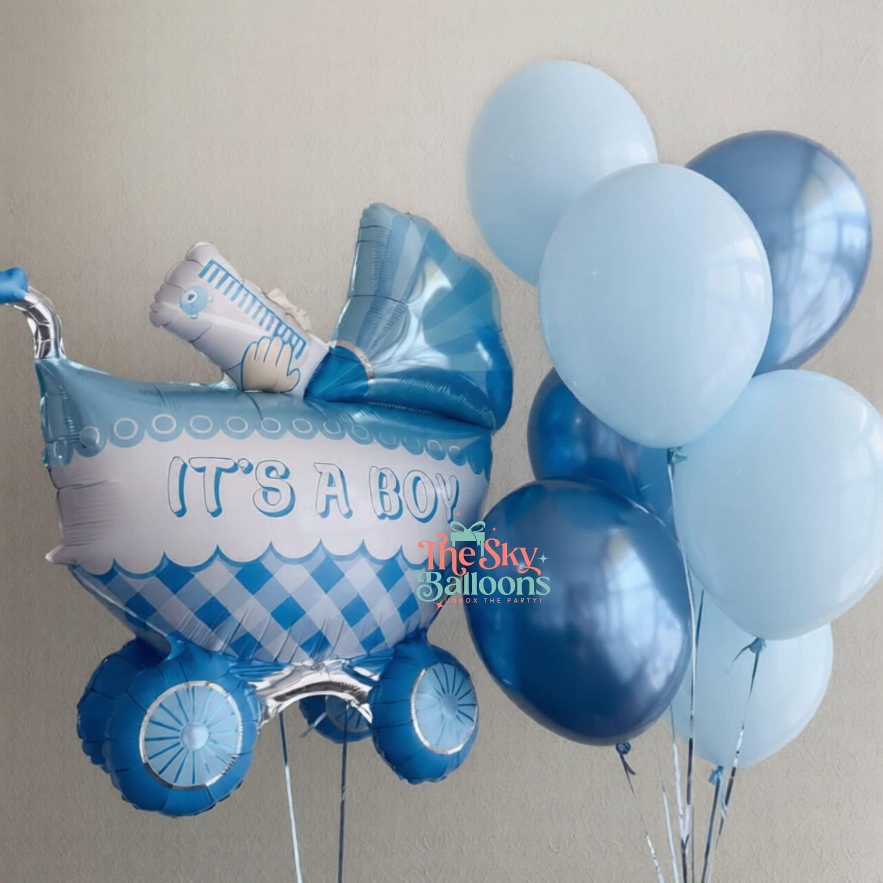 Blue baby shower balloons with 'It's a Boy' message and stroller balloon against a neutral background.