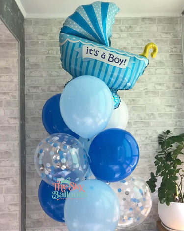 Balloon arrangement with 'it's a Boy!' message against a gray brick wall.