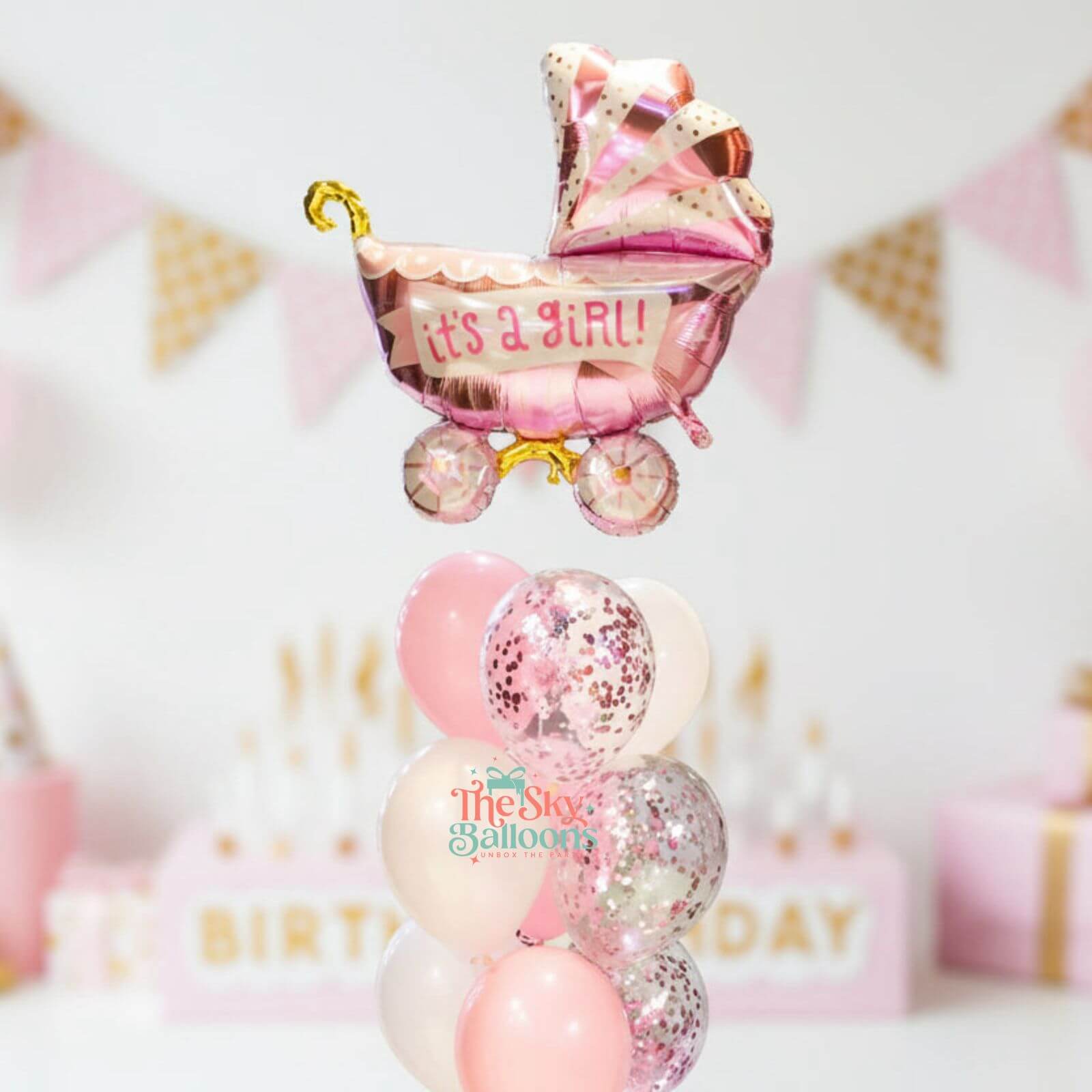 Pink baby carriage balloon with 'It's a Girl!' text, surrounded by other balloons and decorations.