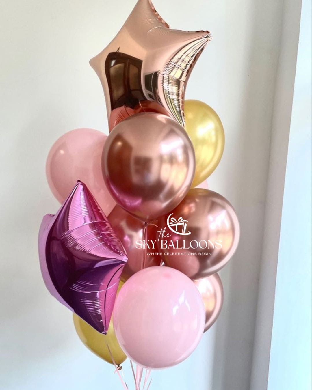Celebration balloon bouquet with pink, metallic rose-gold and gold latex balloons, plus rose-gold and purple star-shaped foil balloons.