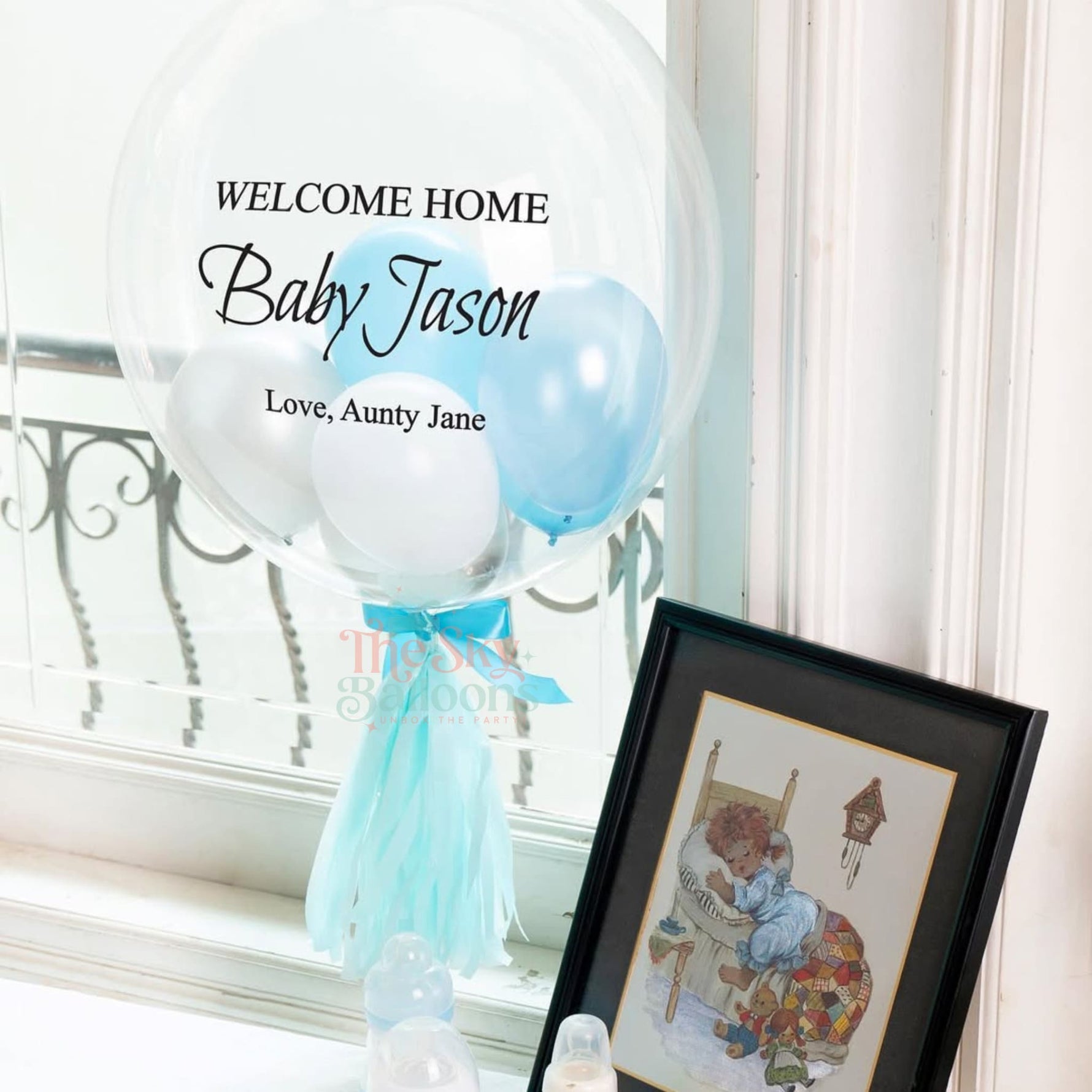 Decorative balloons with 'Welcome Home Baby Jason' text next to a framed picture on a window sill.