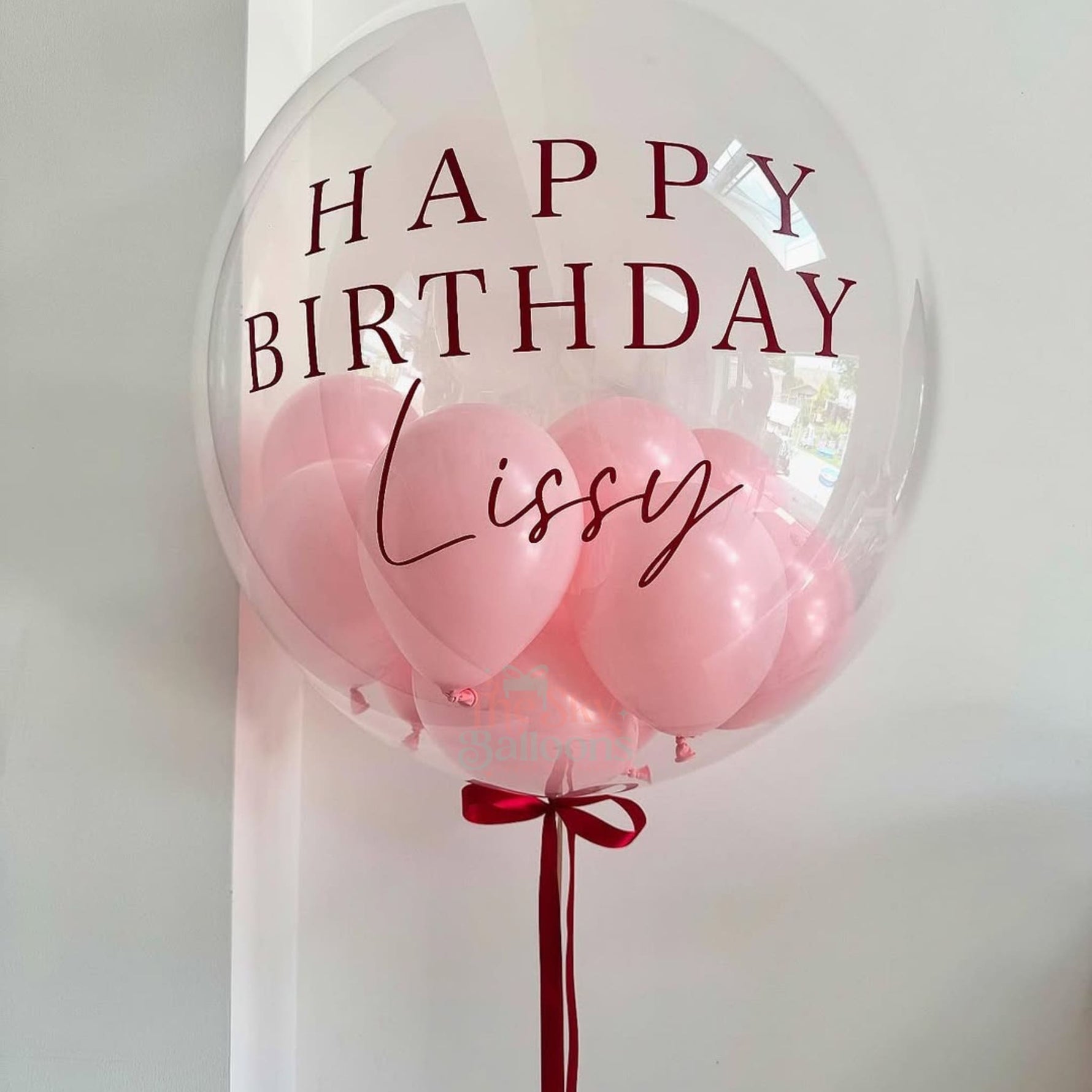 Clear balloon with pink balloons inside and 'Happy Birthday Lissy' text on a white background
