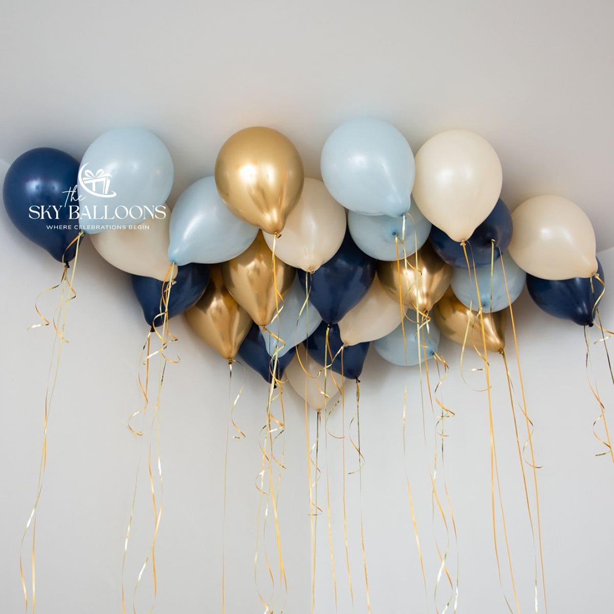 Navy-blue, pale-blue, cream and chrome-gold helium ceiling balloons with hanging gold curling ribbons.