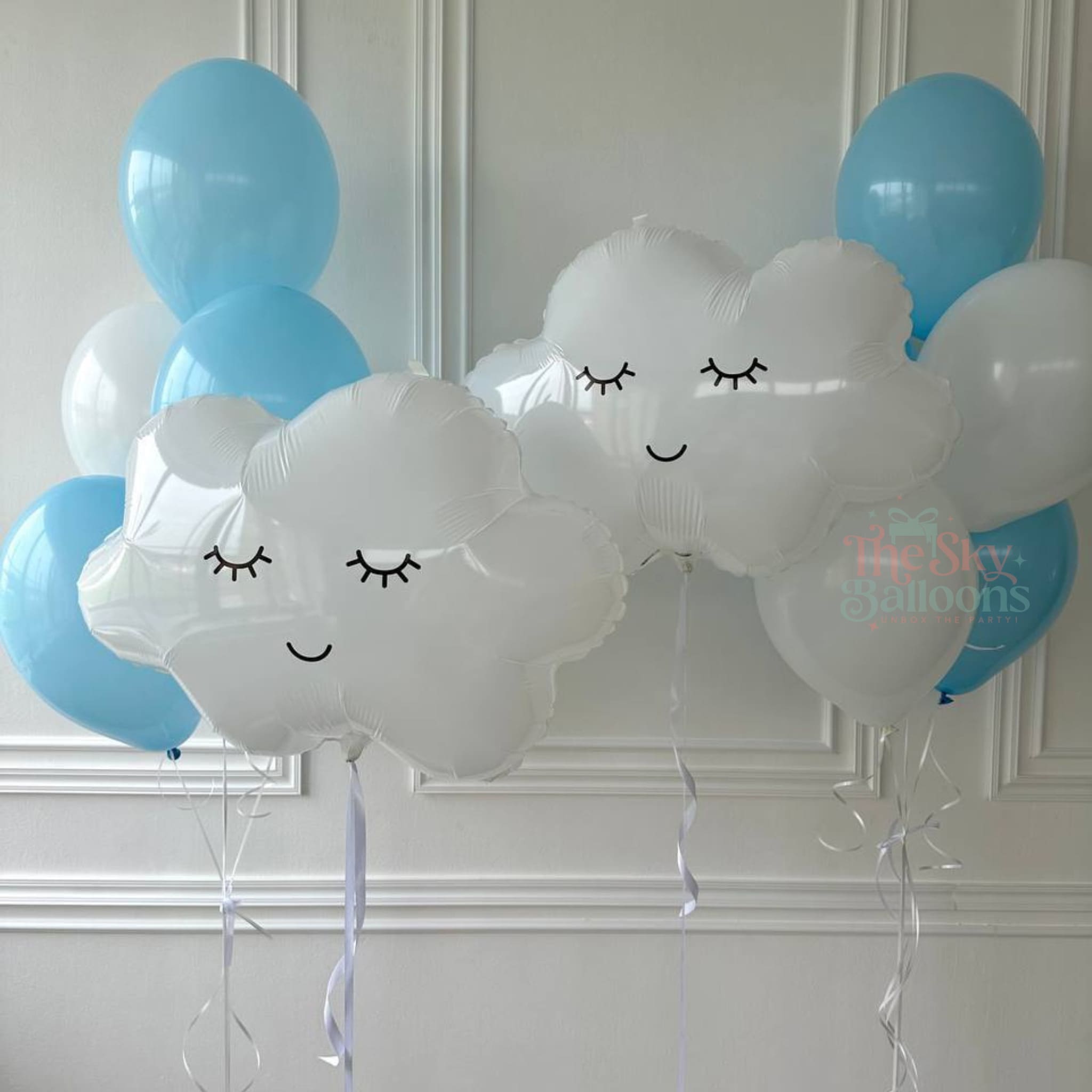 White cloud-shaped balloons with blue and clear balloons against a white wall.