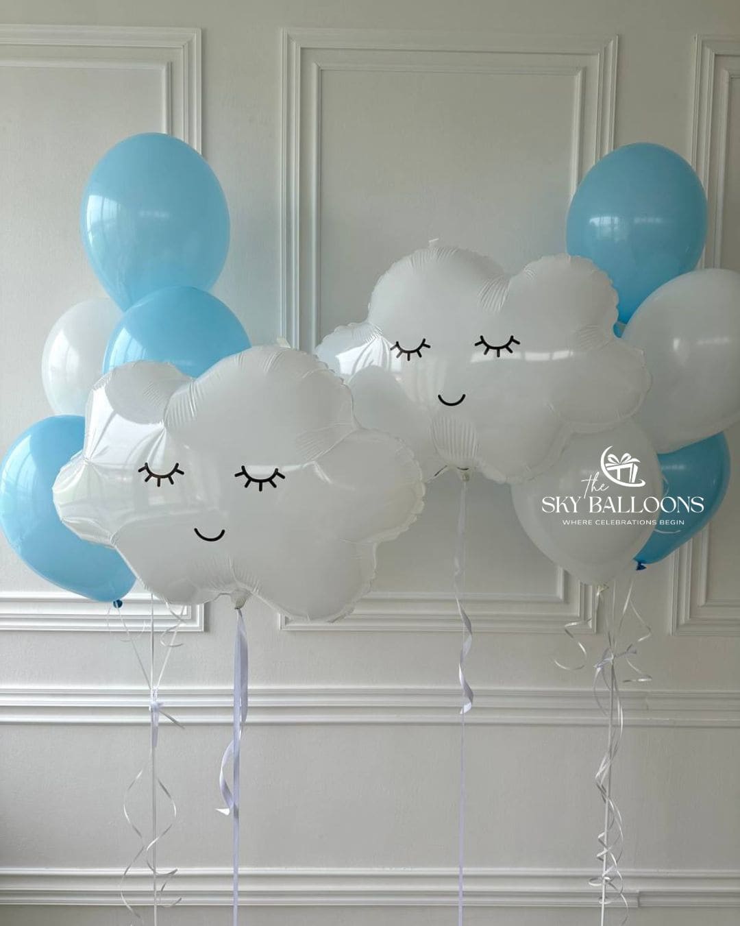 Two balloon bouquets featuring smiling white cloud foil balloons with blue and white latex balloons and trailing white ribbons.
