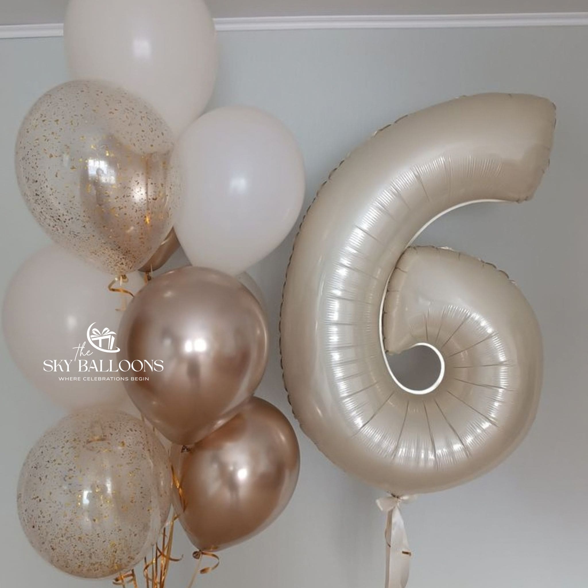 Champagne number 6 foil balloon beside a bouquet of white, metallic champagne and clear gold confetti balloons with gold ribbons.